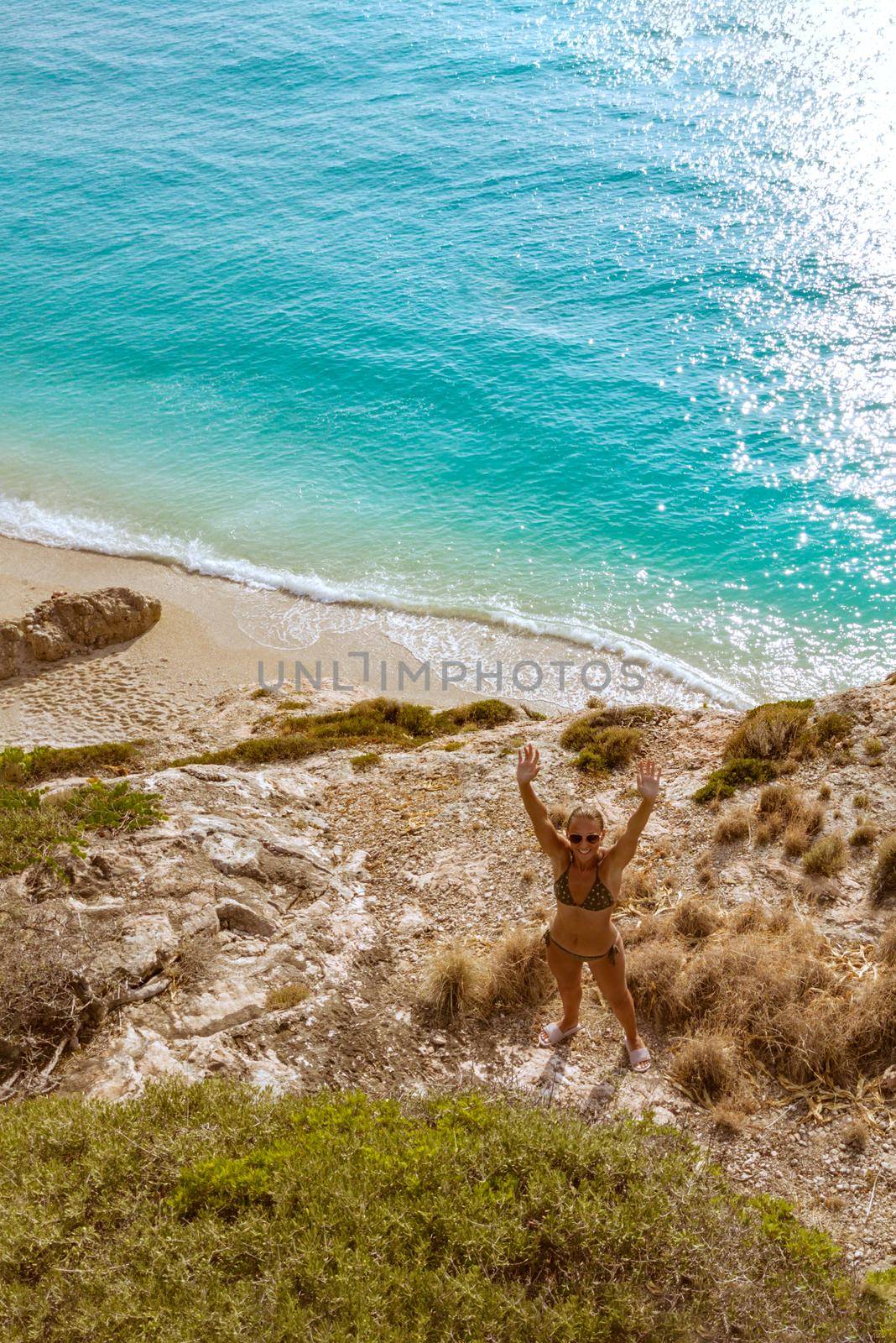 Top view of a beautiful woman enjoying in sunbath on the beach in a bikini, relaxing near clear sea water. She is waving and looking at camera.