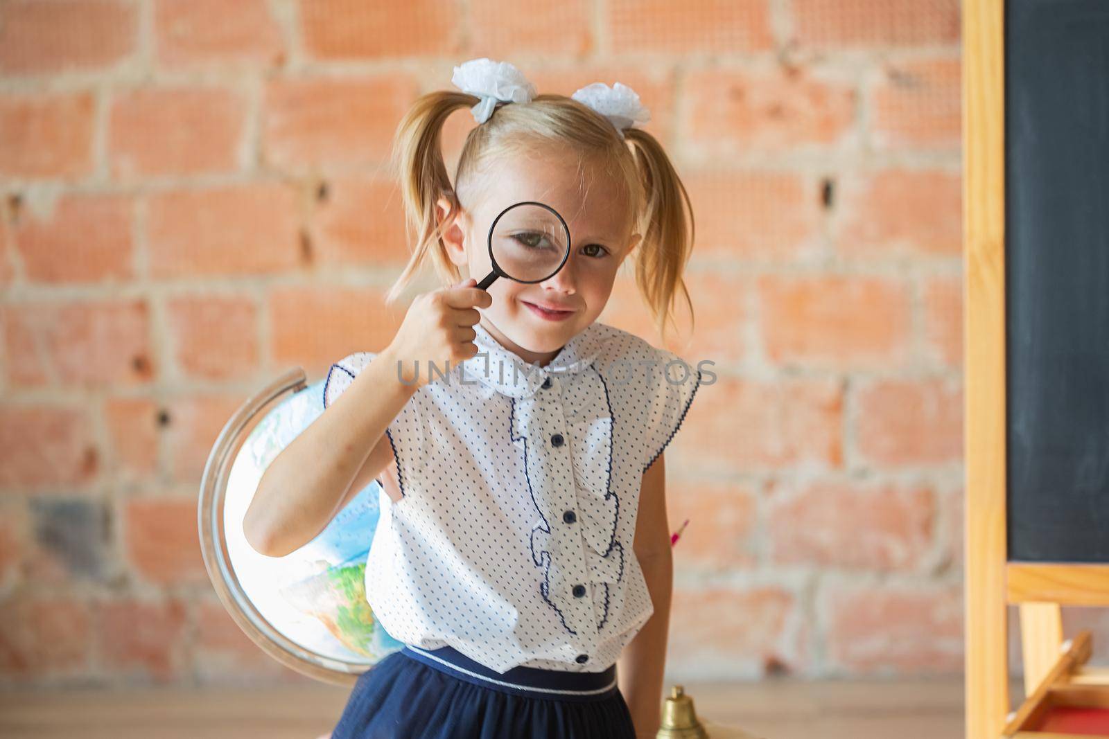 Adorable caucasian private school kindergarten girl with magnifier if front of her eye, back to school concept