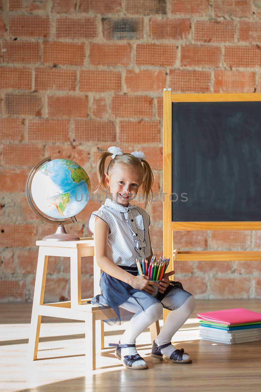Portrait of caucasian school kindergarten girl standing in front of blackboard with pencils in her hands, back to school concept