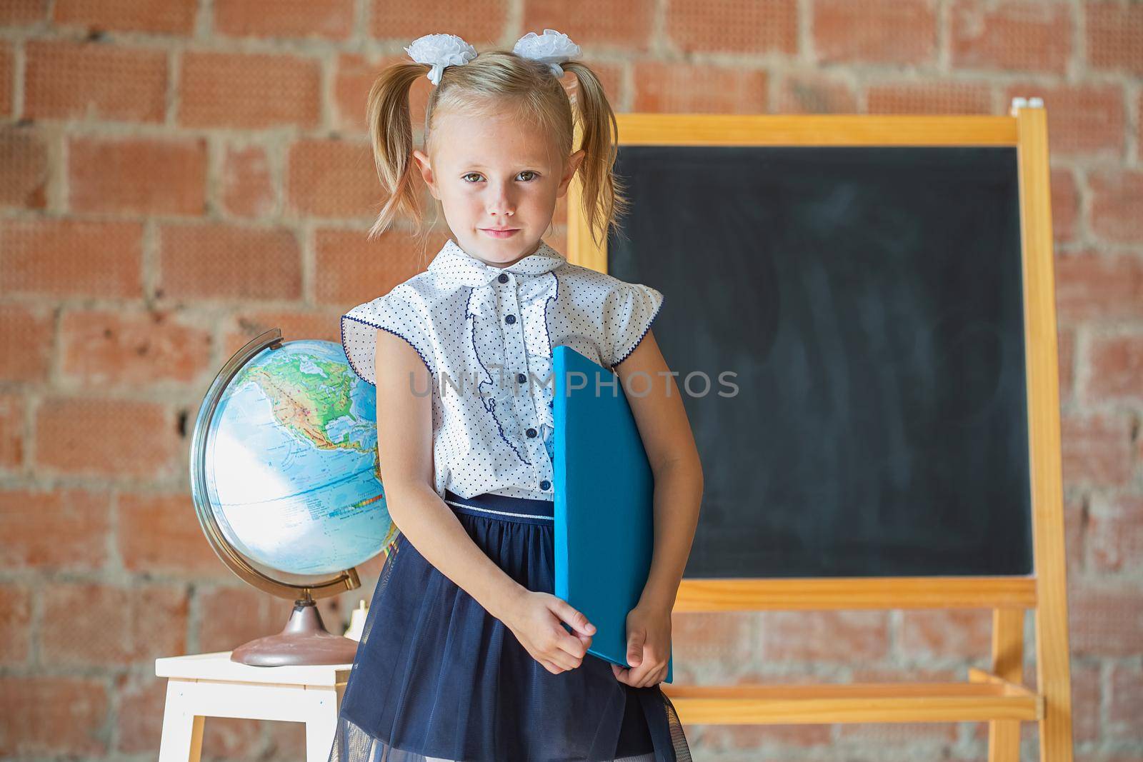 Unhappy little girl in school uniform with a book in her hands, back to school concept