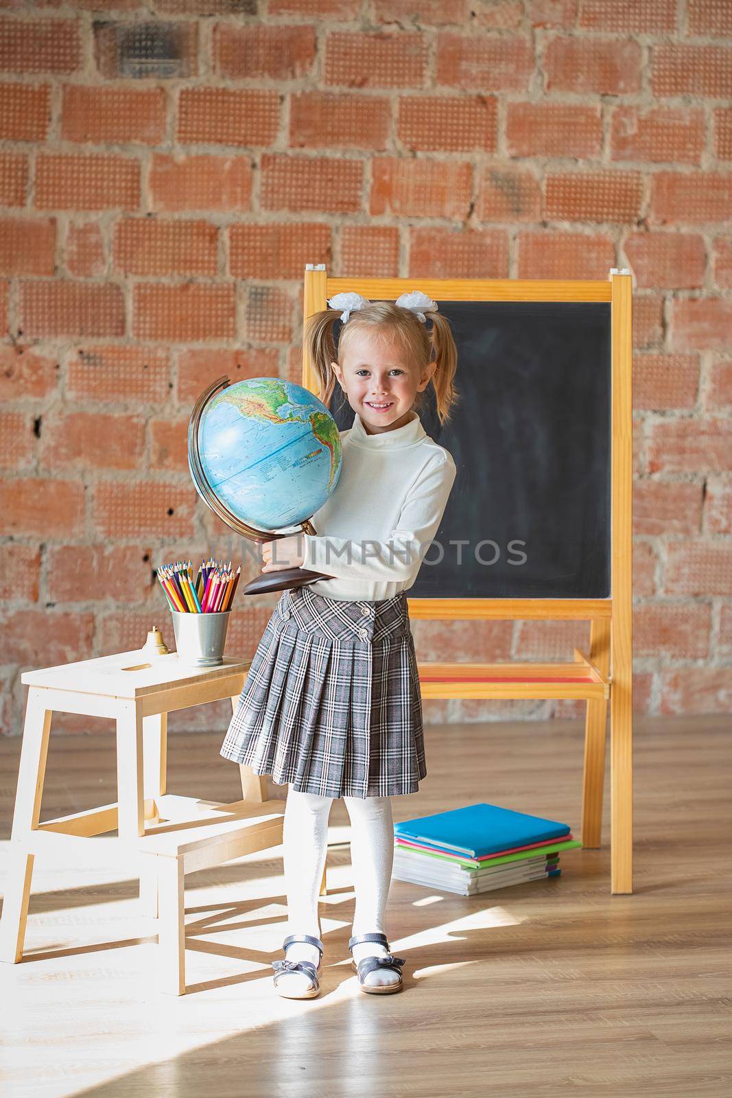 Adorable private schoolgirl in front of blackboard with globe in her hands, back to school concept
