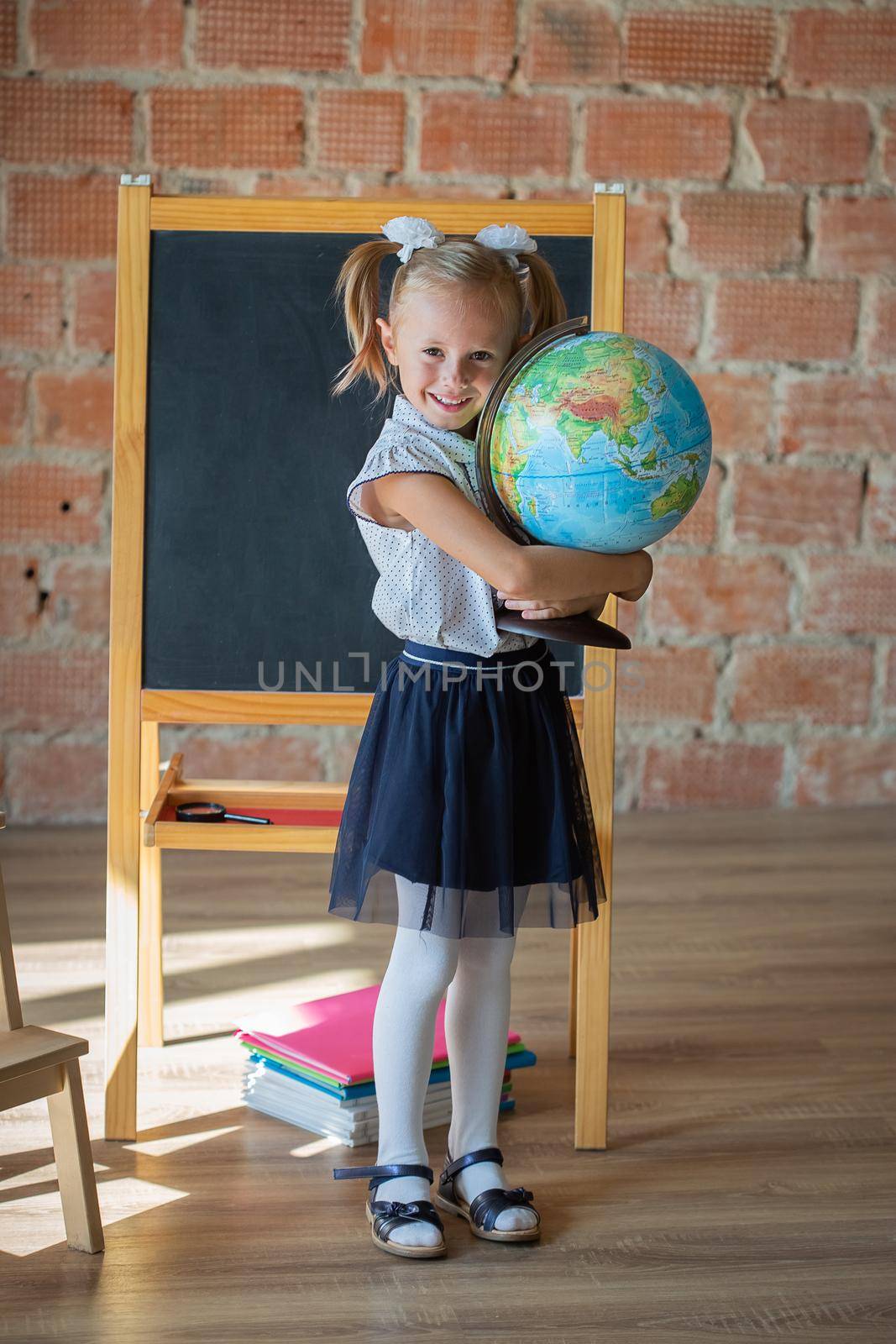 Portrait of caucasian schoolgirl standing in front of chalkboard with globe in her hands, back to school concept
