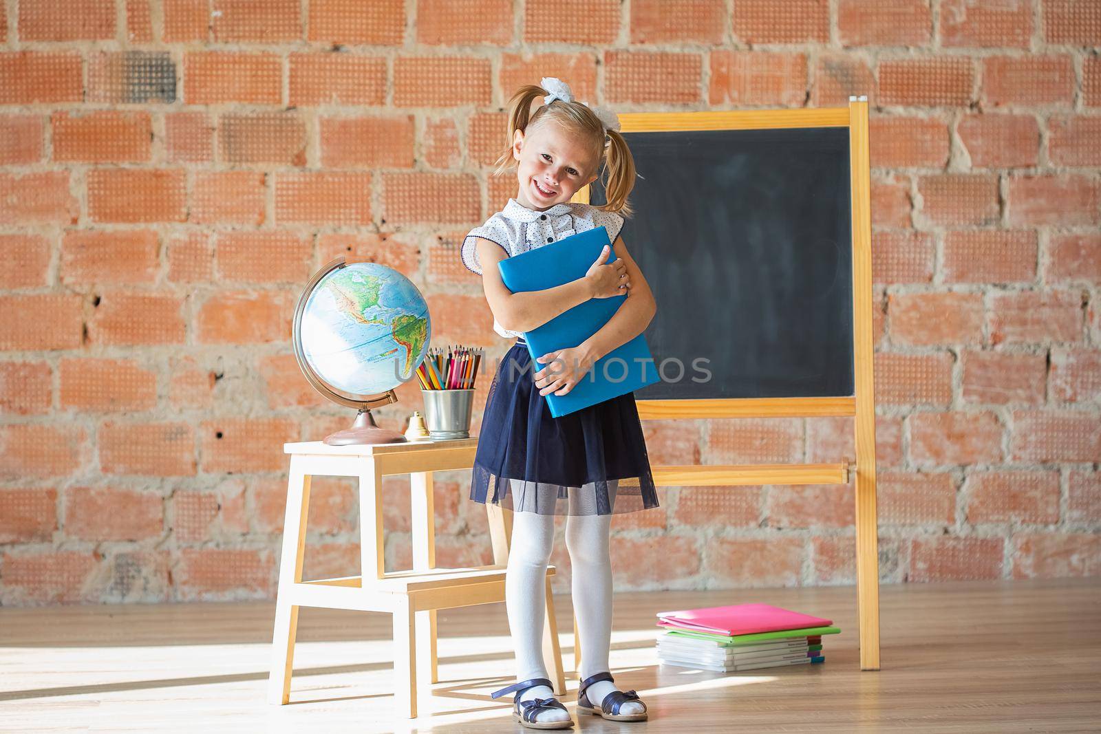 Adorable school girl smiling in front of blackboard with book in her hands by galinasharapova