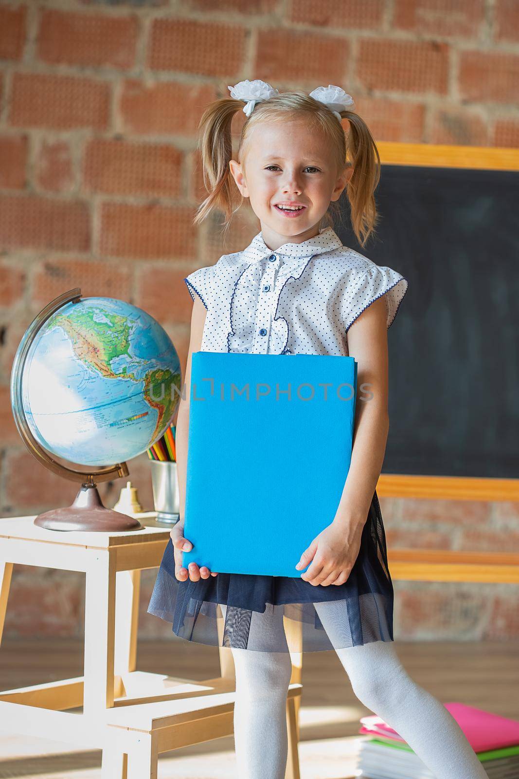 Portrait of schoolgirl standing in front of chalkboard with book in her hands by galinasharapova