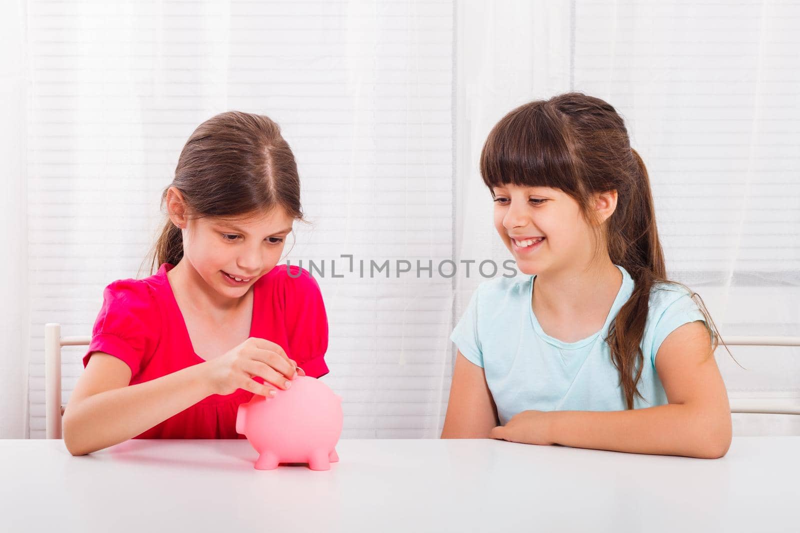 Cute little girls putting coin into piggy bank. Children's savings