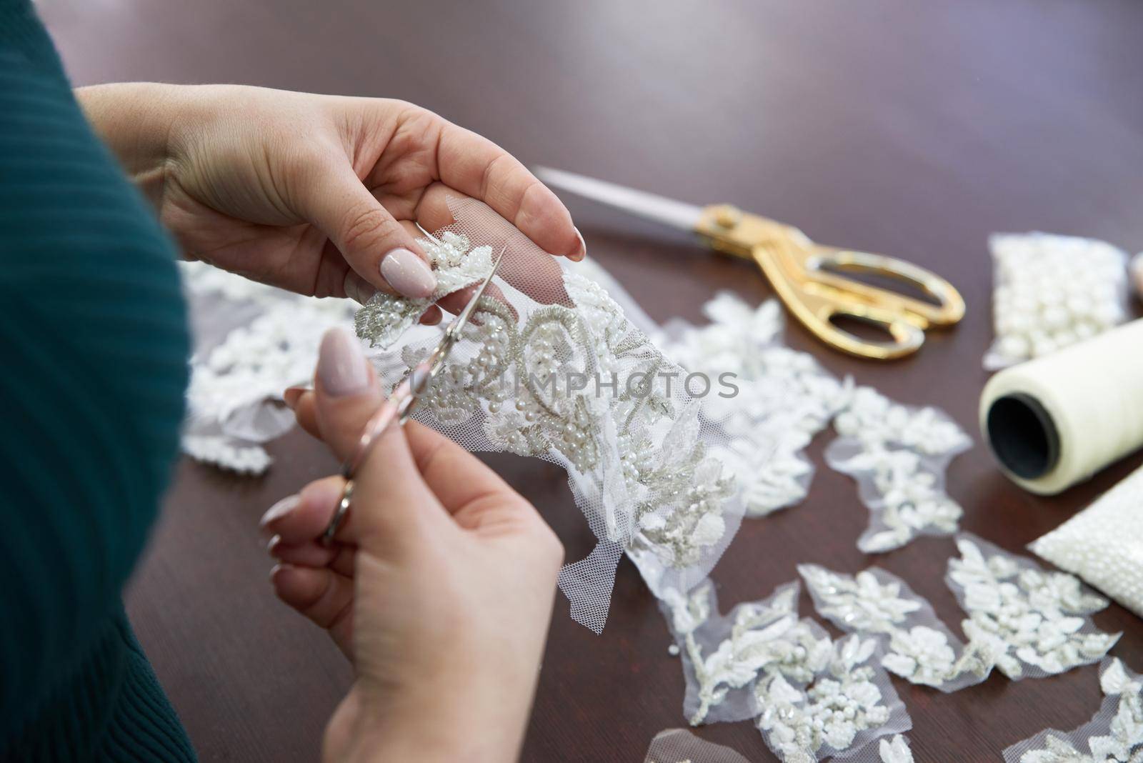 selective focus of seamstress sitting at table, sewing machine and cutting lace with scissors in sewing studio