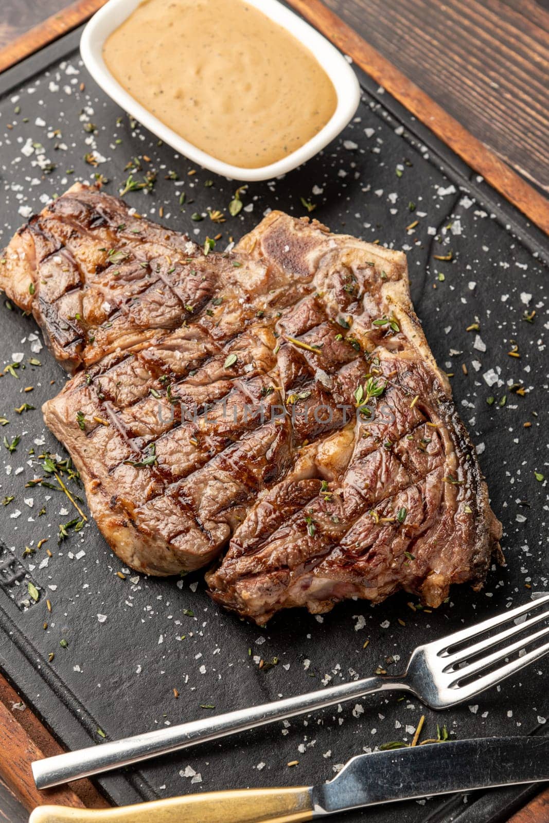Grilled tomahawk steak on stone cutting board in steakhouse restaurant by Sonat