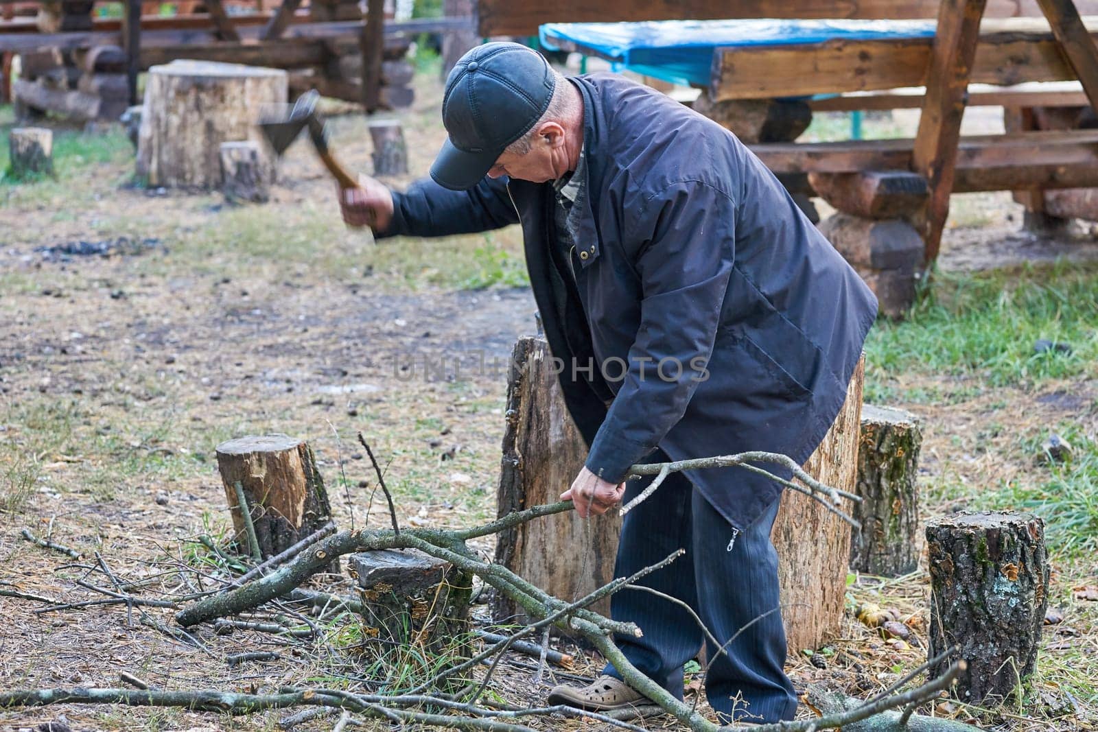 Elderly retired man chopping firewood with an ax, cooking grilled food on a fire by jovani68
