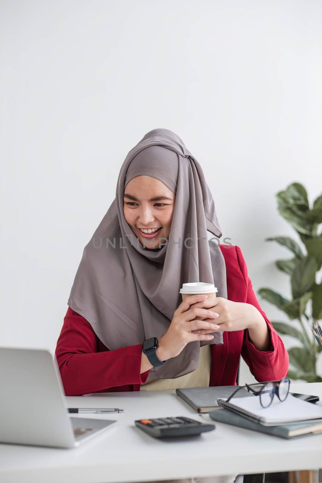 Portrait of beautiful muslim businesswoman smiling at the camera, sitting at her desk. by wichayada