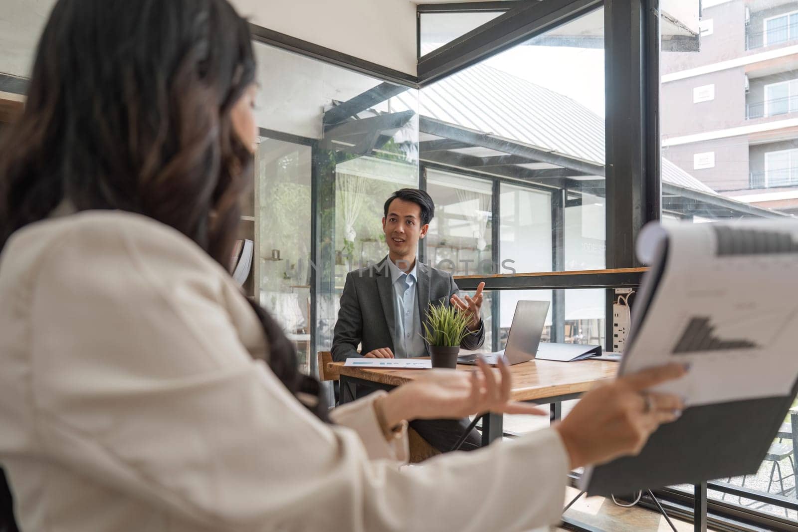 Two business people talk project strategy at office meeting room. Businessman discuss project planning with colleague at workplace while having conversation and advice on financial data report.