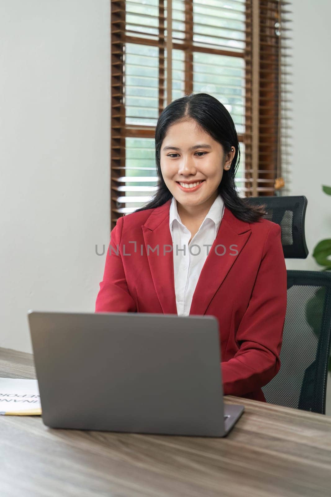 Portrait of beautiful smiling young businesswoman sitting at bright in office modern work and typing on laptop by nateemee