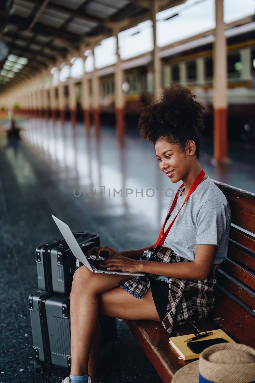 Asian teenage girl african american traveling using computer laptop while waiting for a train at a station. by Manastrong