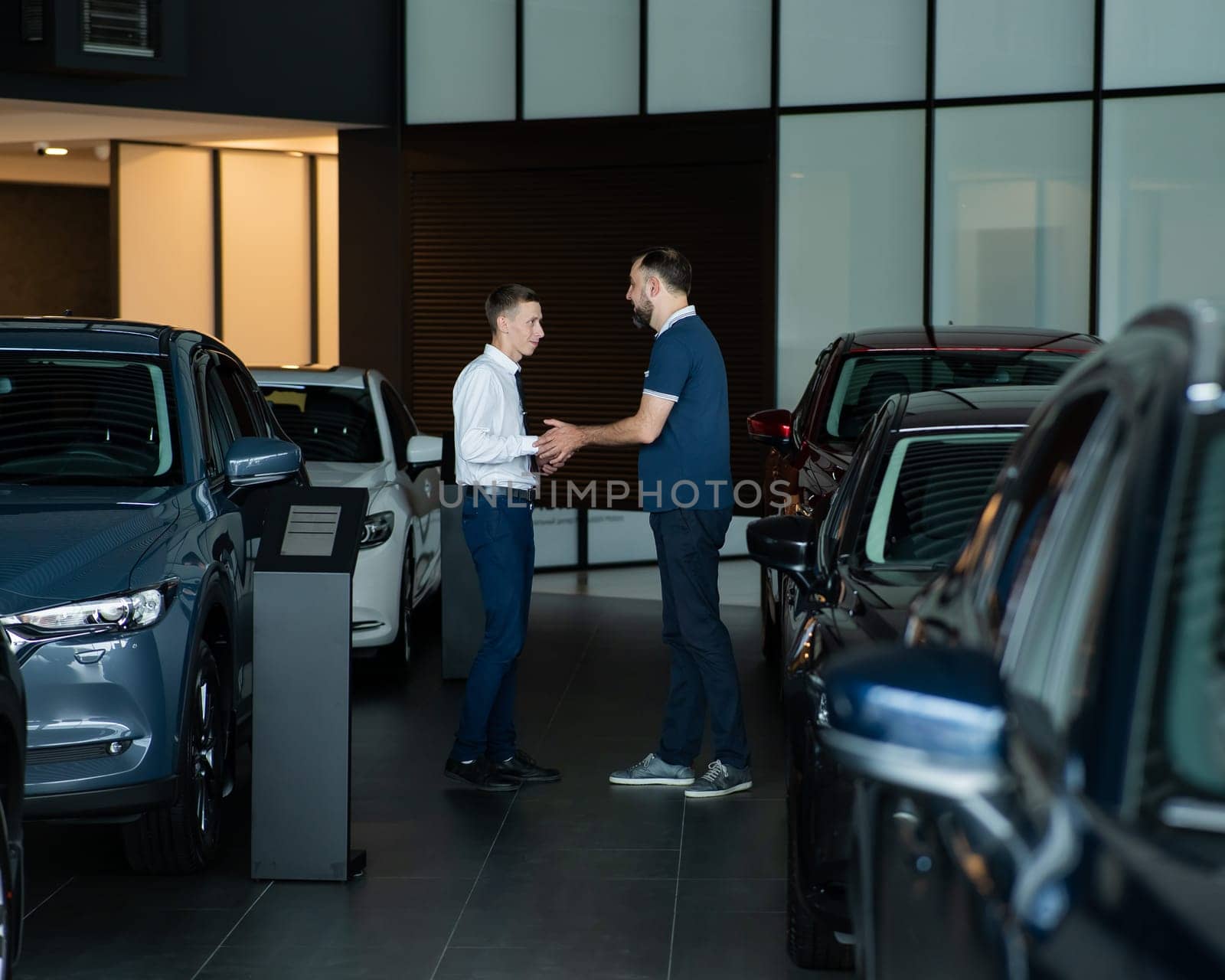 Seller and buyer shake hands in a car dealership. Caucasian man buys a car. by mrwed54
