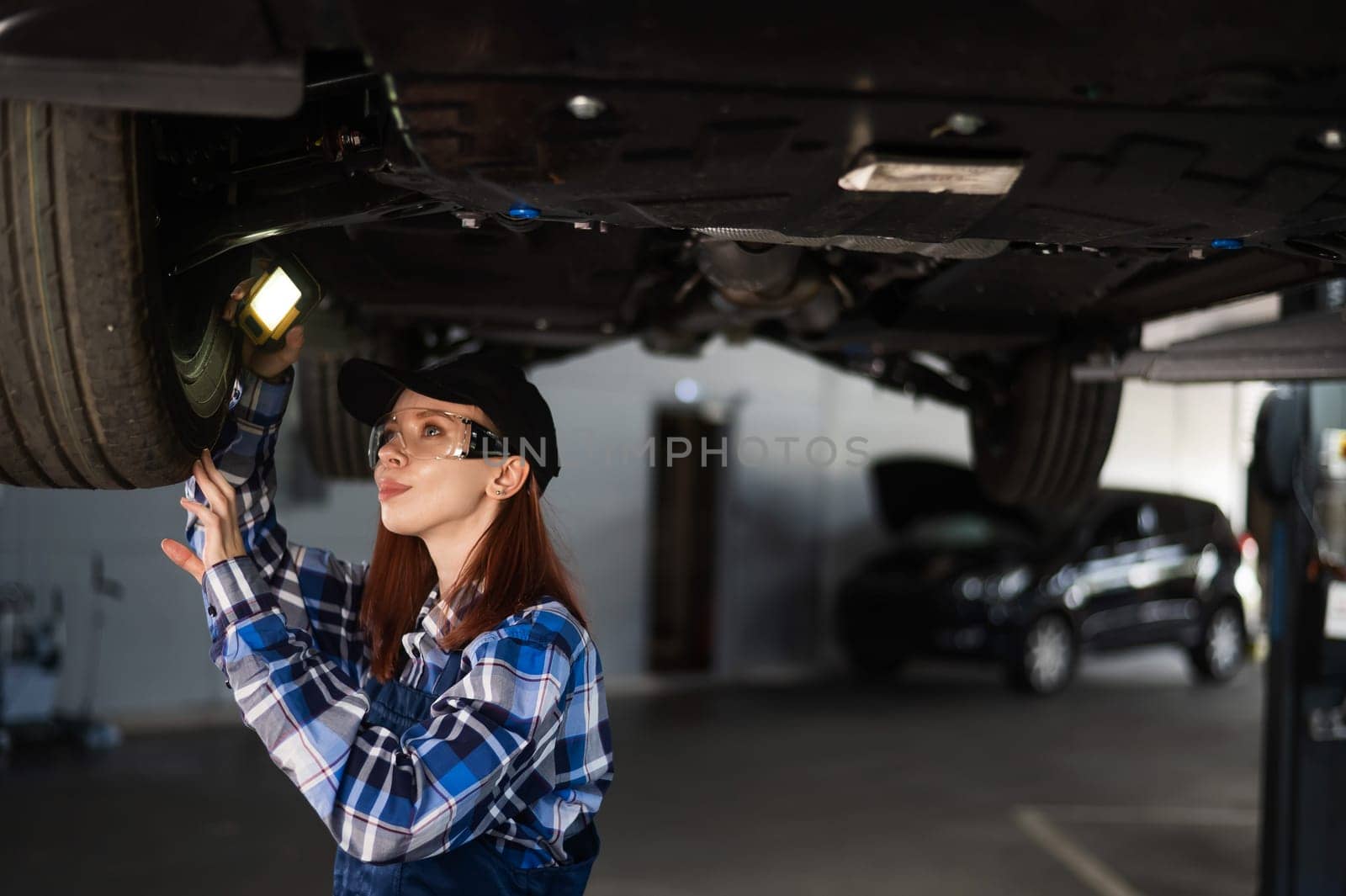 A female mechanic inspects a lifted car. A girl at a man's work