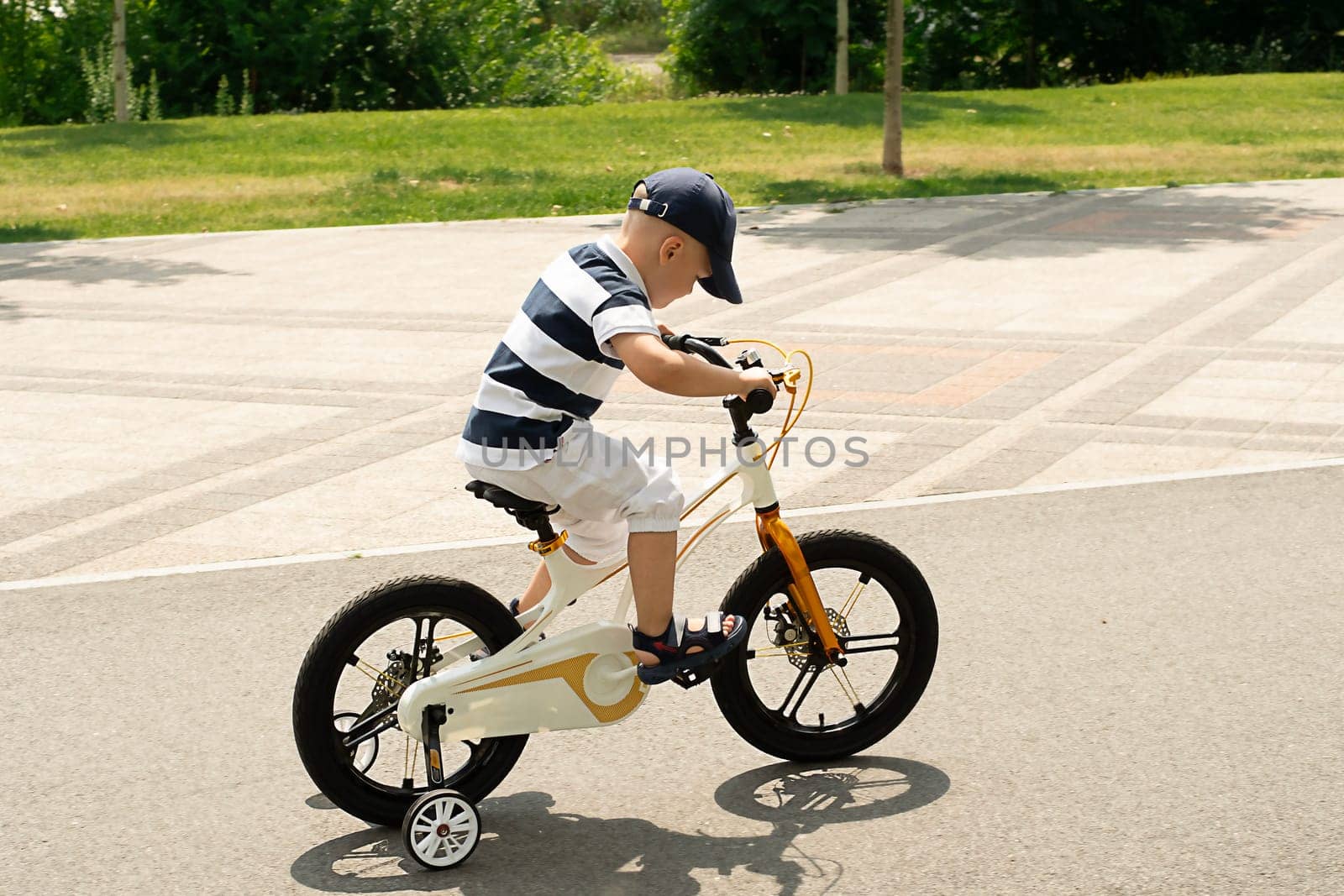 Sport concept. Boy on a bike. A small beautiful, happy, Caucasian boy 4 years old in a cap and a striped T-shirt rides a bicycle along the bike path in the summer outdoors.