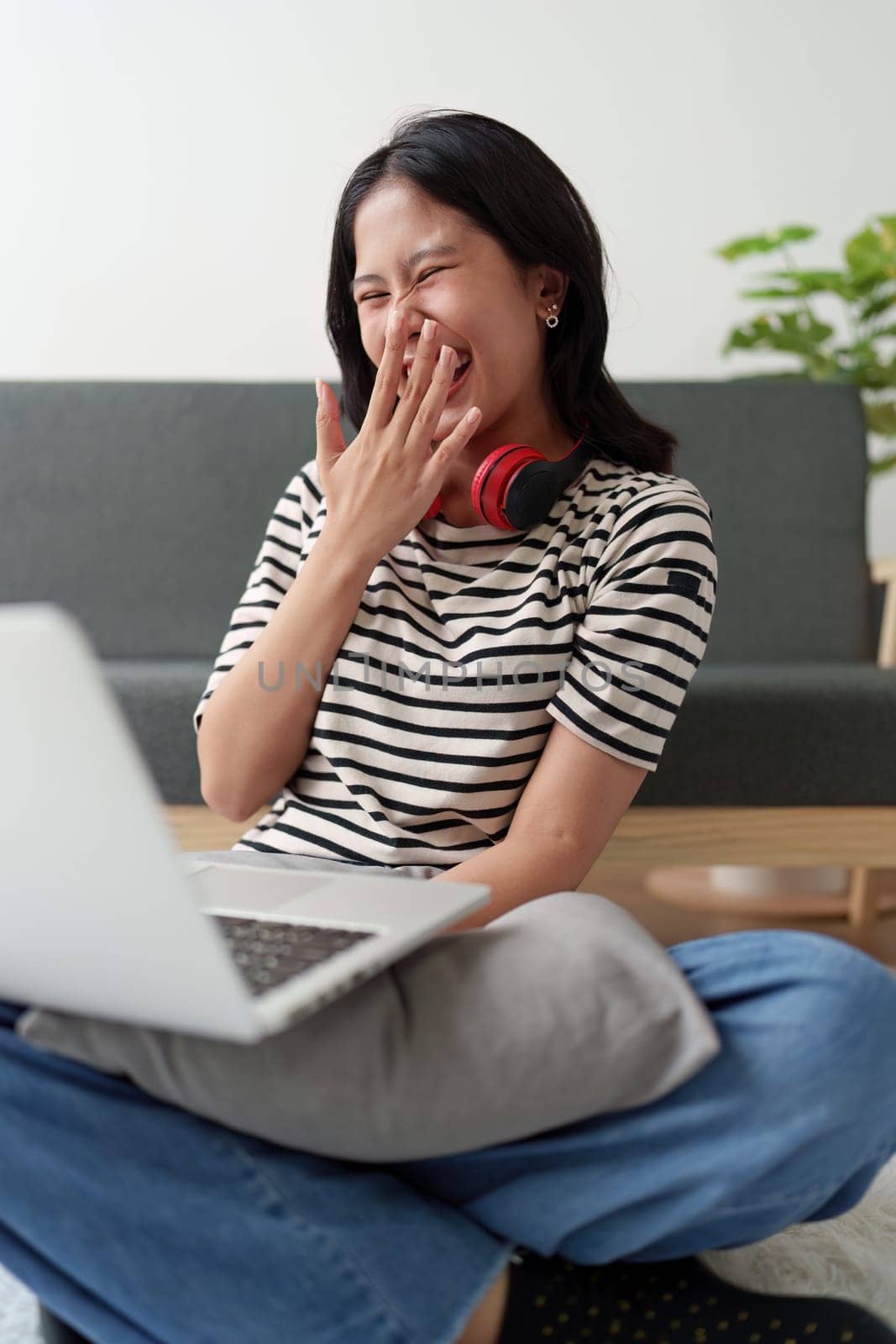 Young asian relaxed smiling pretty woman relaxing with laptop at home. Female feeling joy enjoying with mobile phone on cozy couch.