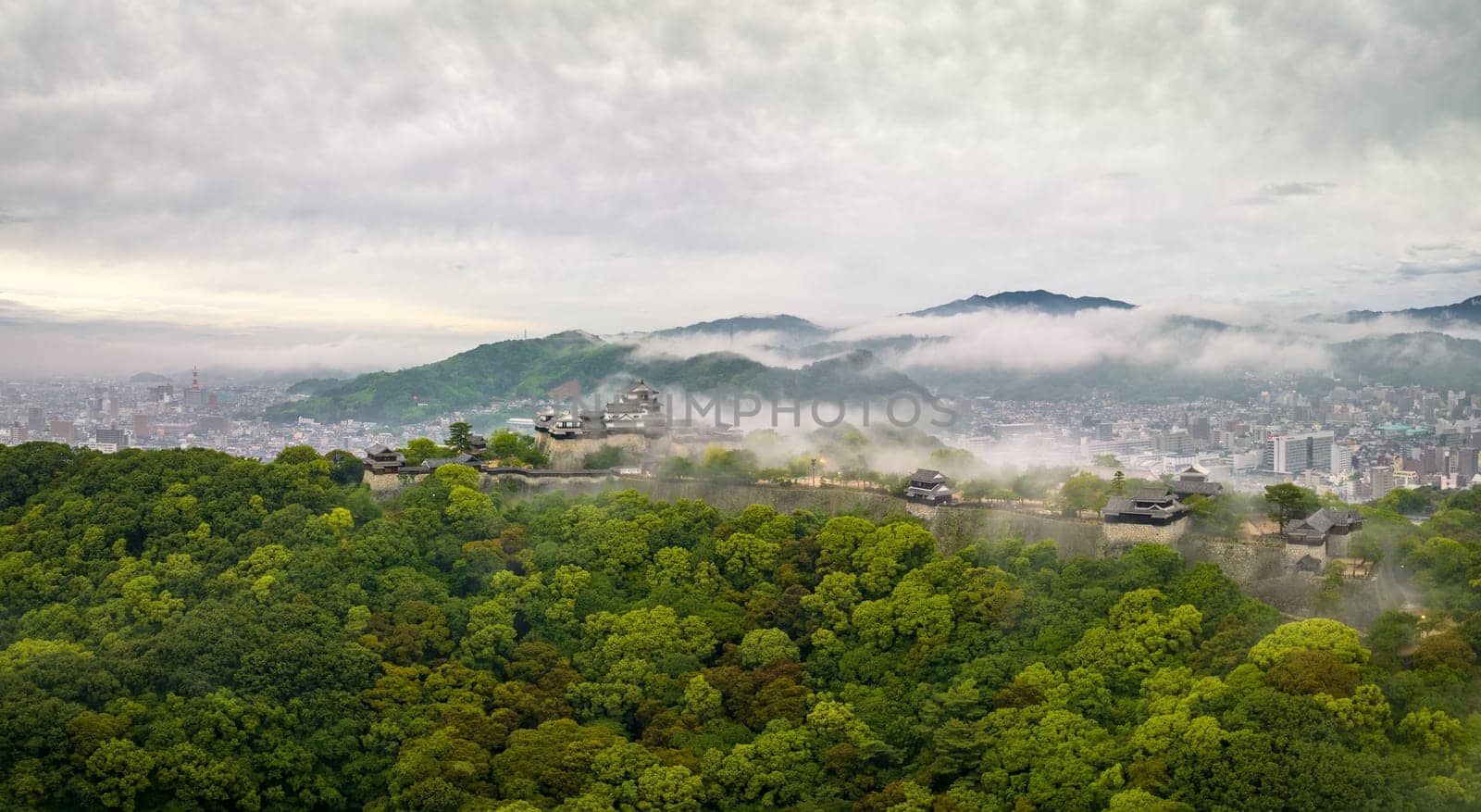 Aerial view of early morning fog over Matsuyama Castle on hill by city by Osaze