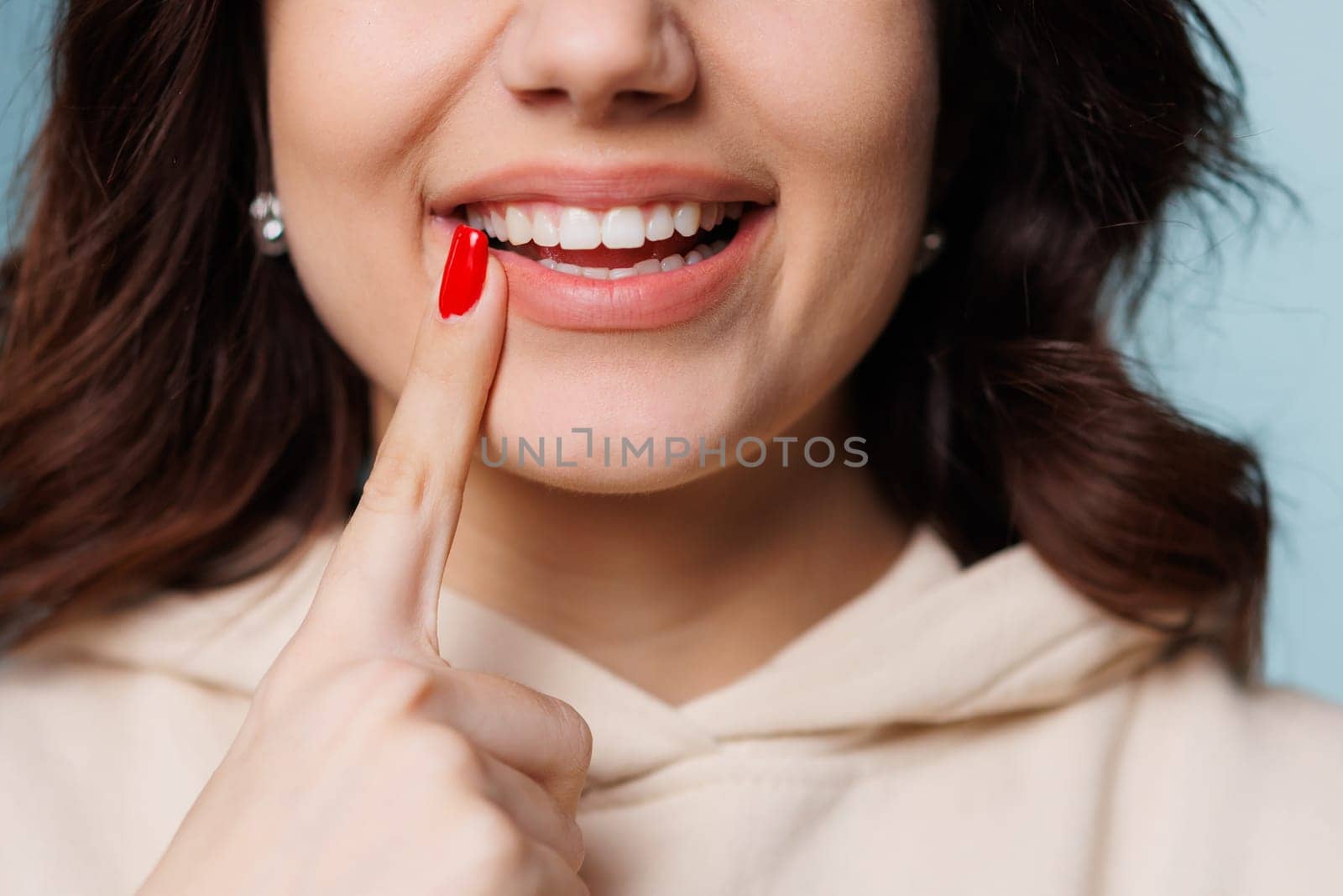 Happy girl showing toothy smile, pointing finger at healthy white teeth. Clinic patient satisfied with dentist service, enamel cleaning, whitening, dental care, correction. Cropped shot, close up. High quality photo