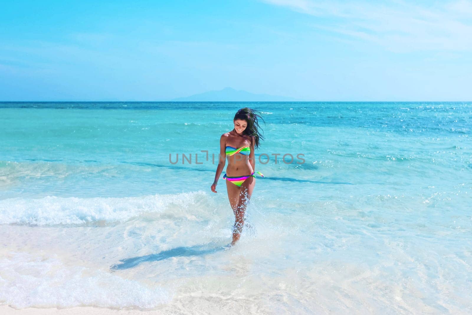 Happy tanned girl in rainbow bikini at seaside, blue sea water on background