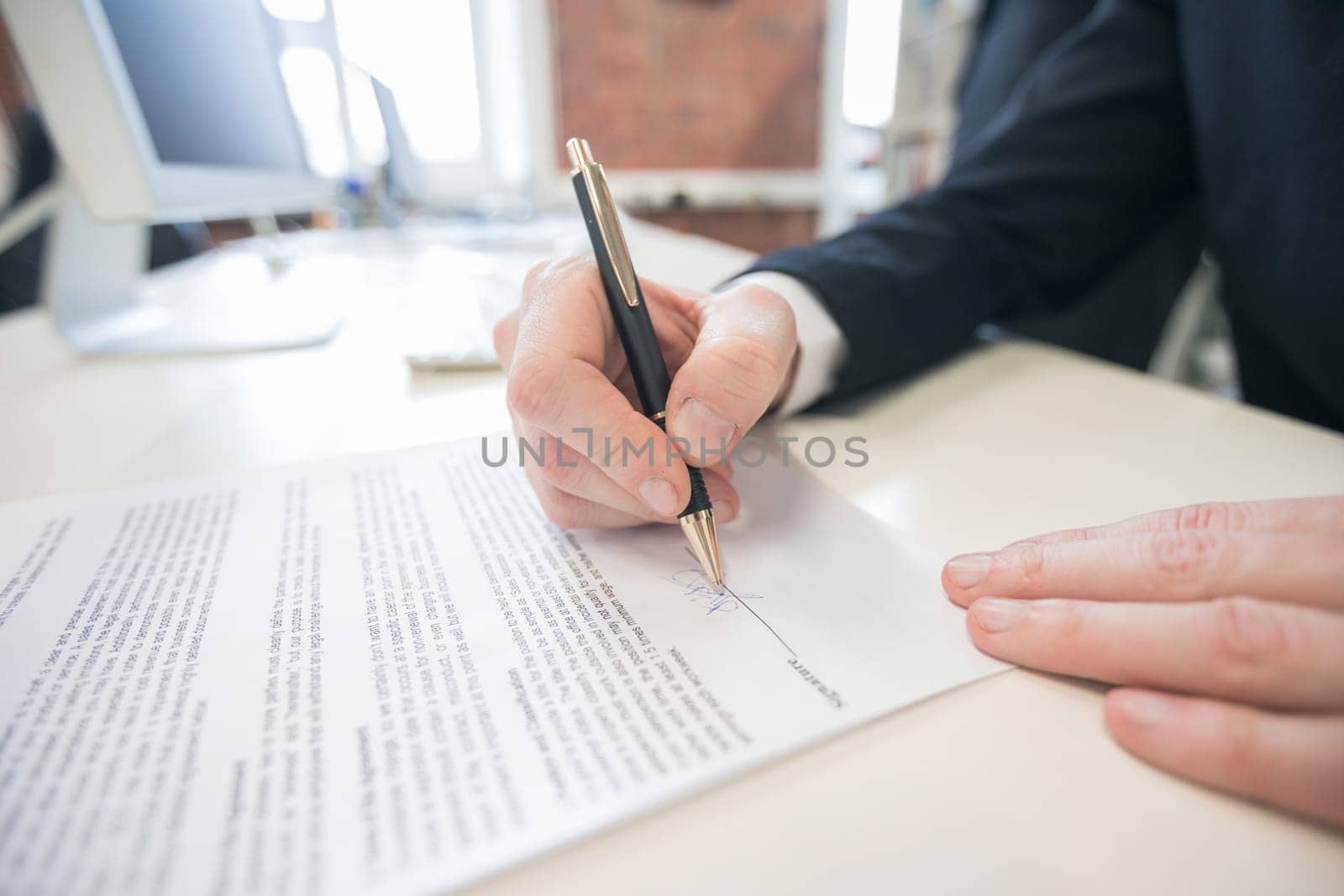 Businessman sitting at office desk signing a contract with shallow focus on signature.