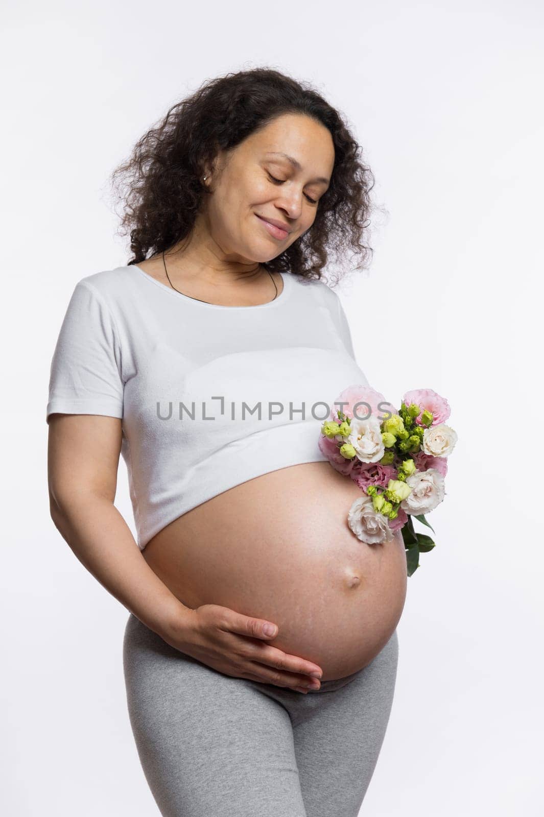 Happy pregnant woman with flowers, caressing her belly, smiles enjoying wonderful moments of her pregnancy and maternity by artgf