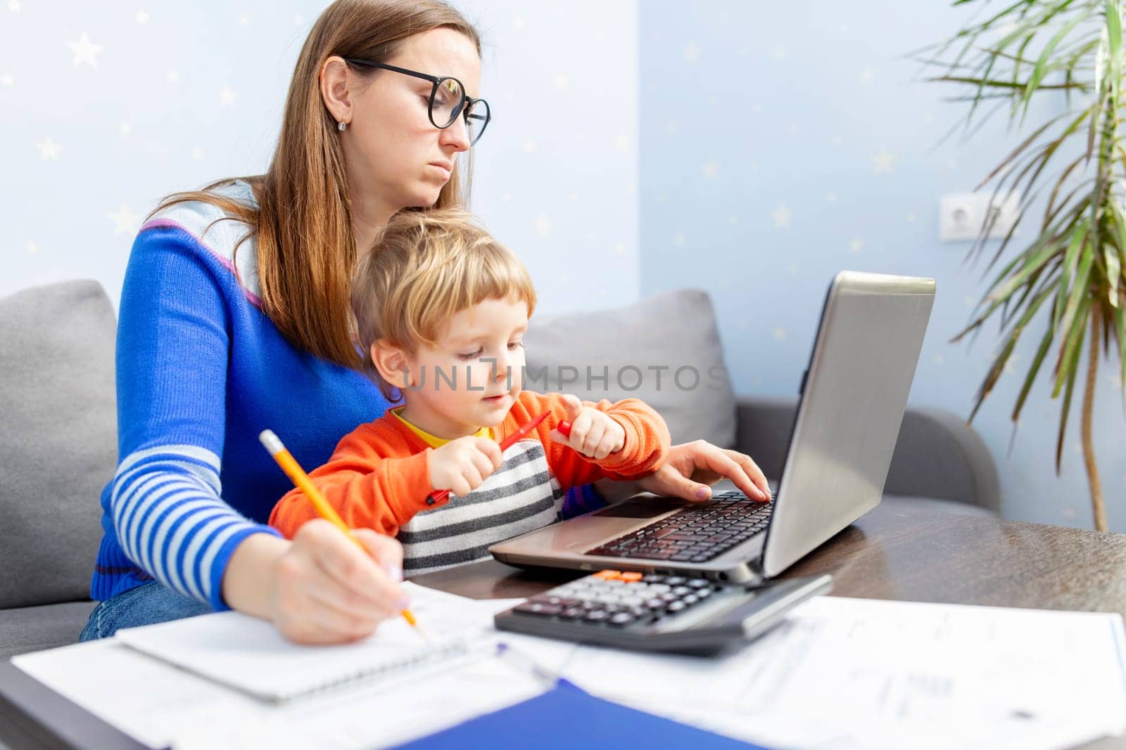 Business woman is working at home on a laptop with her baby. Concept of female business, working mom, freelancing, home office. Lifestyle moment.