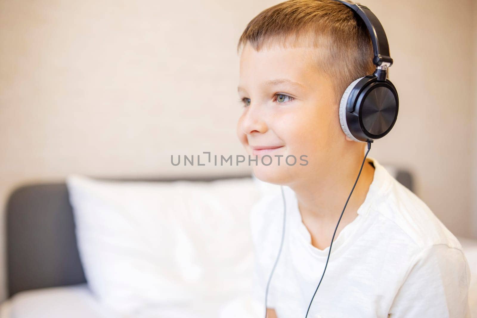 A boy in white T-shirt listening to music with headphones on the bed at home.