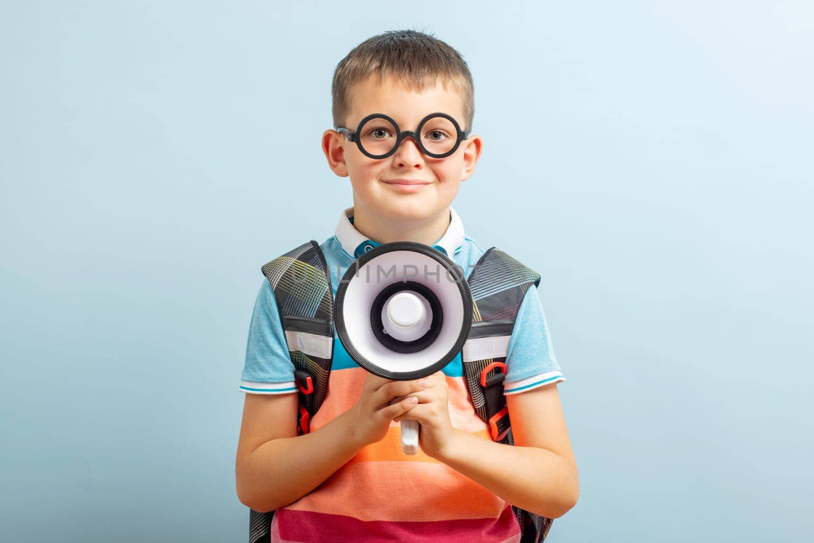 Little schoolboy with megaphone on blue background. Boy with megaphone making an announcement with copy space.
