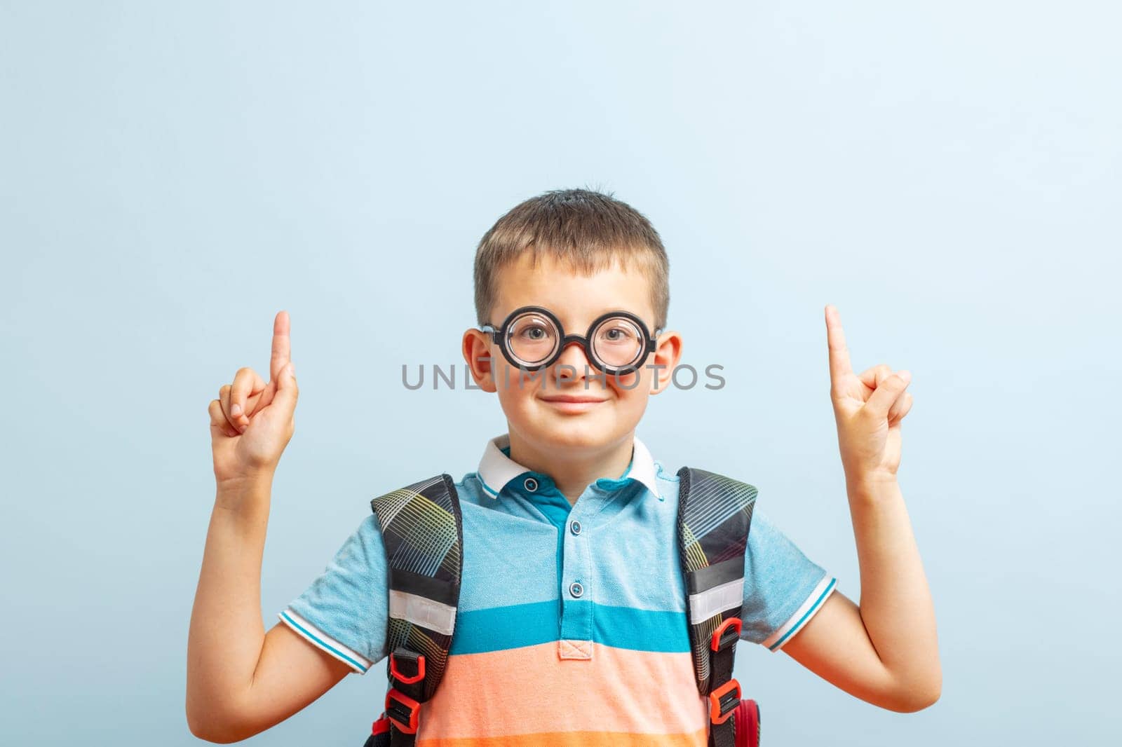 Happy school boy pointing fingers up showing something on blue background in studio. Free space for your text. Back to school.