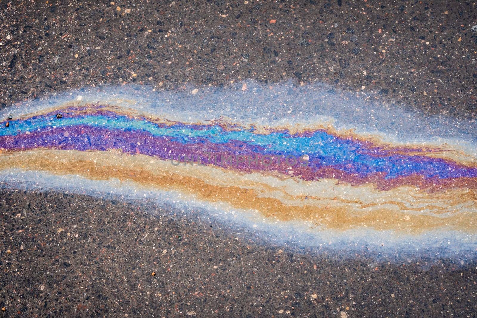 Rainbow puddle of spilled oil product on the road. Environmental pollution concept