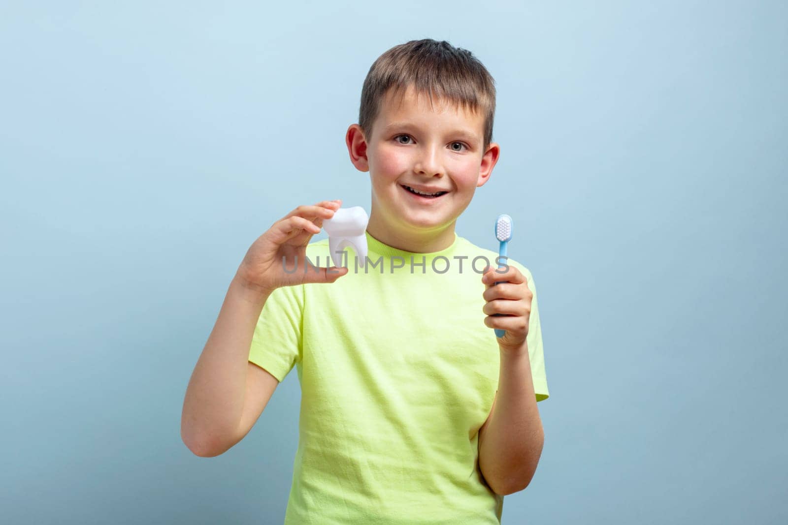 Child holds big tooth and toothbrush on a blue background. Caring for teeth. Dentistry and healthcare concept. Healthy teeth concept.