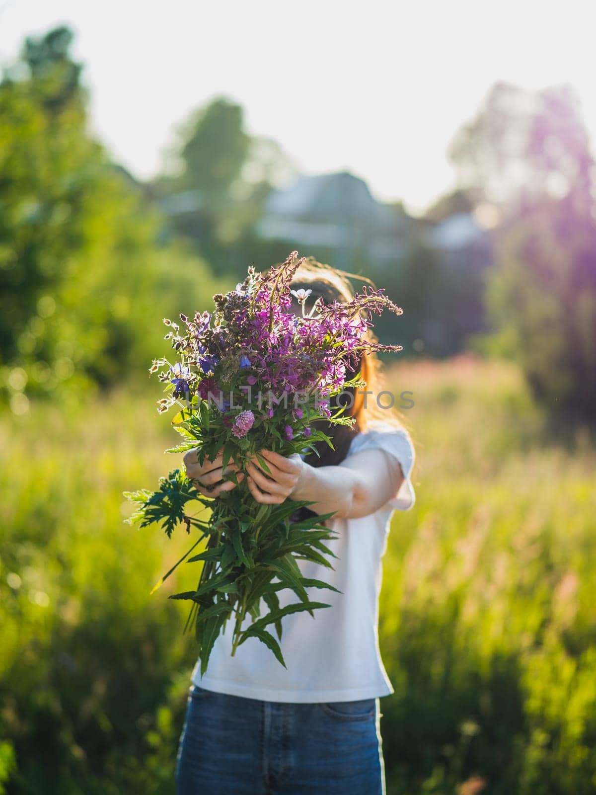 Young woman holds wild flowers bouquet outdoors by fascinadora