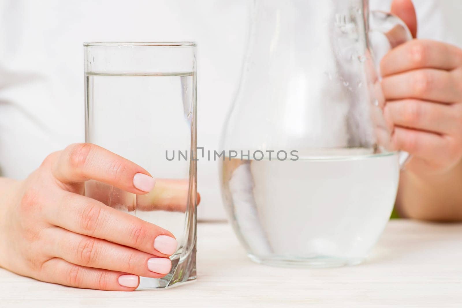 A female is pouring fresh, clear water from a jug into a glass. Health and diet concept. Clean water for good health.