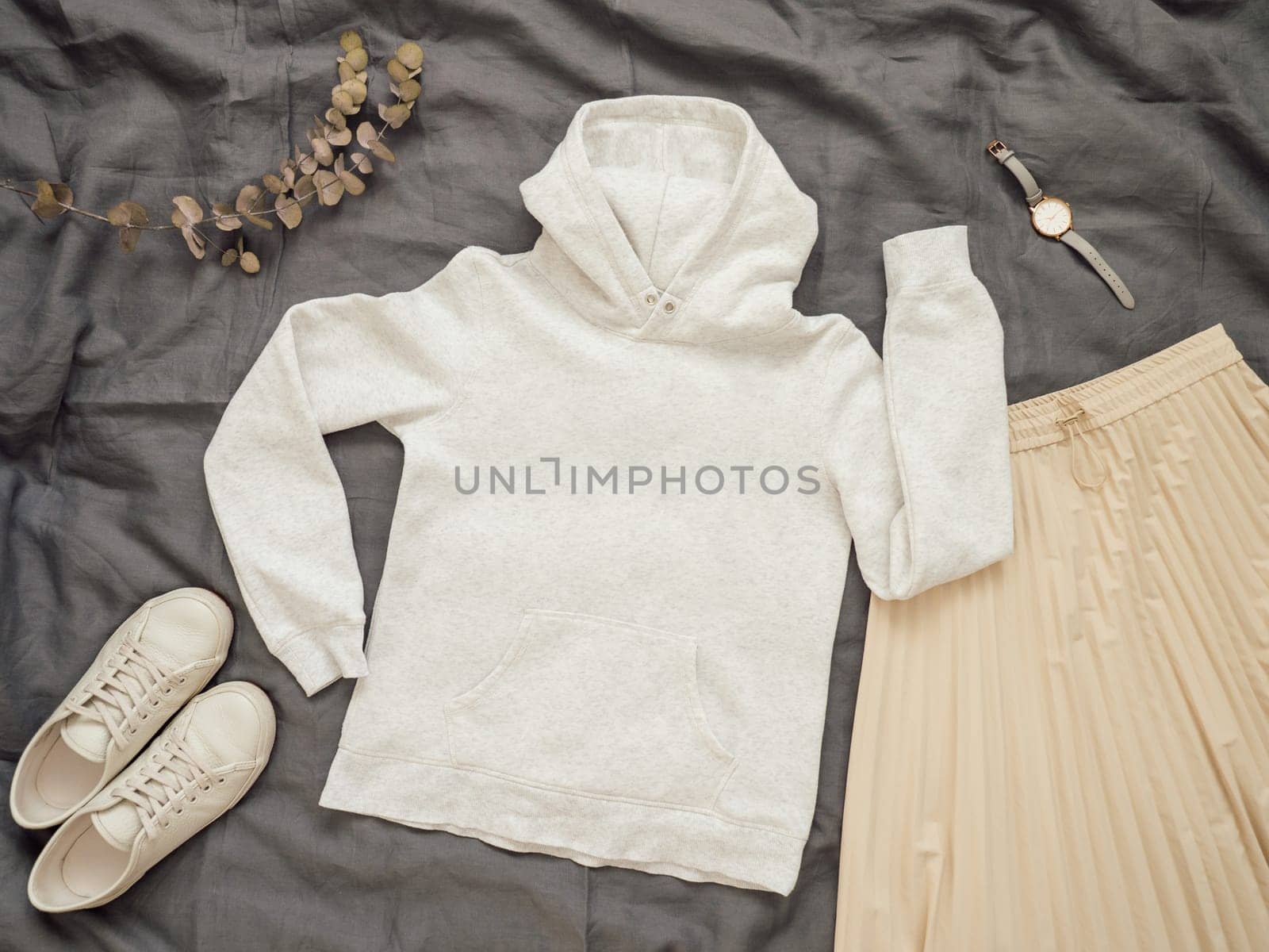 Fashionable female look with white empty hoody, cream pleated skirt and white sneakers. Top view of white blank hoody with long sleeves over gray bed linen. Mock up for hoody print design.