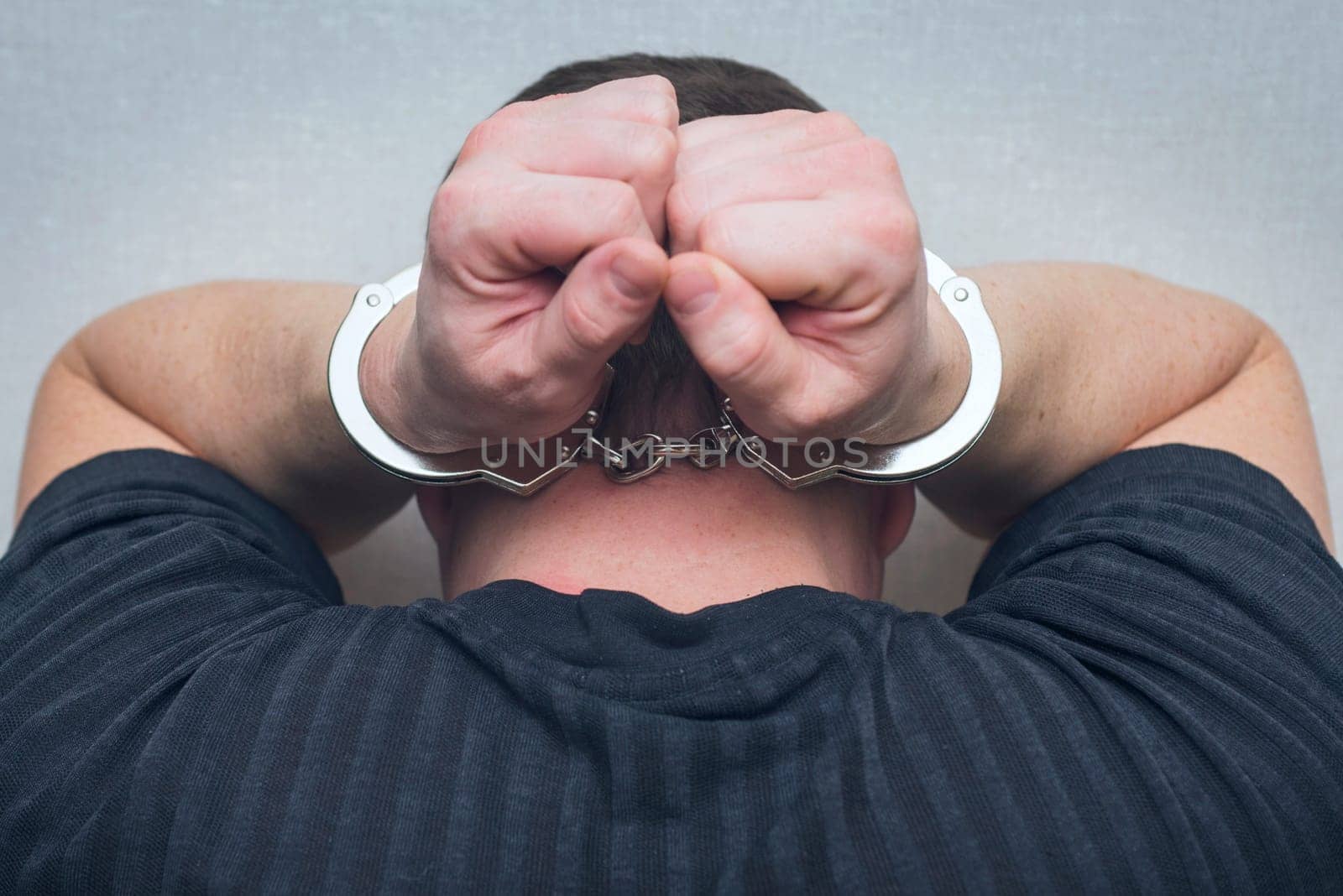 Criminal in handcuffs. Arrested man with hands in handcuffs behind his head.