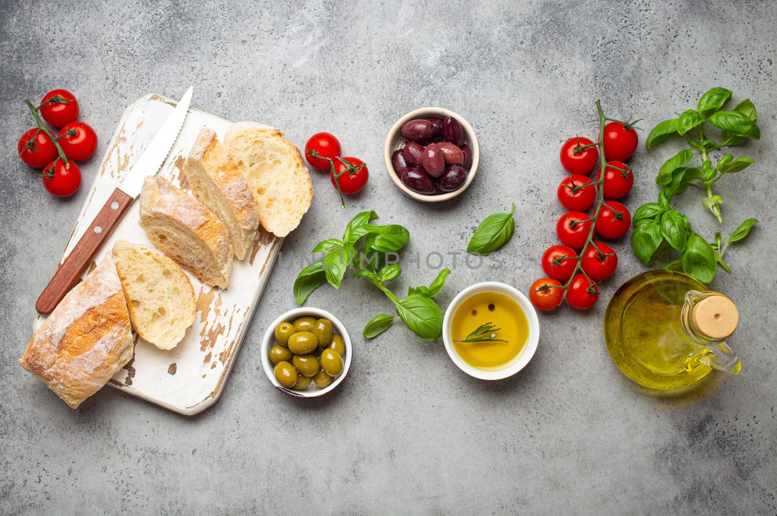 Food composition with sliced ciabatta, olives, olive oil, spaghetti, fresh basil, cherry tomatoes on gray concrete stone rustic background top view. Italian cuisine concept by its_al_dente