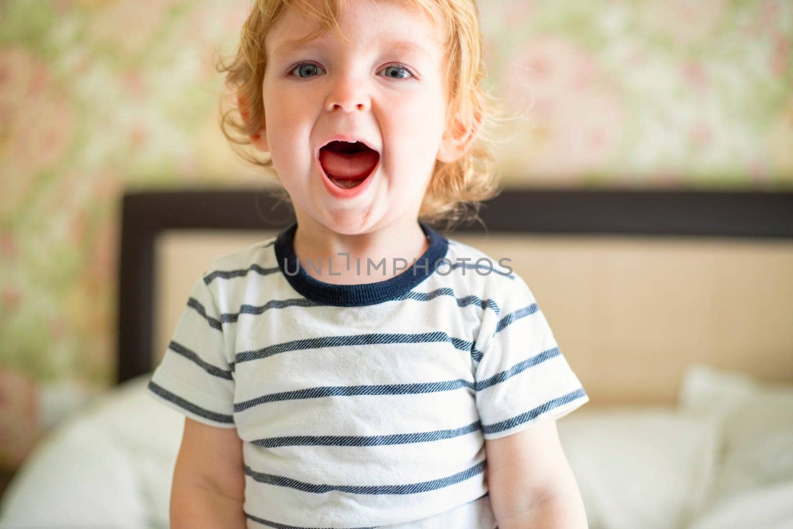 Cute laughing child boy sits in bed. Boy plays at home. Child in a sunny bedroom.