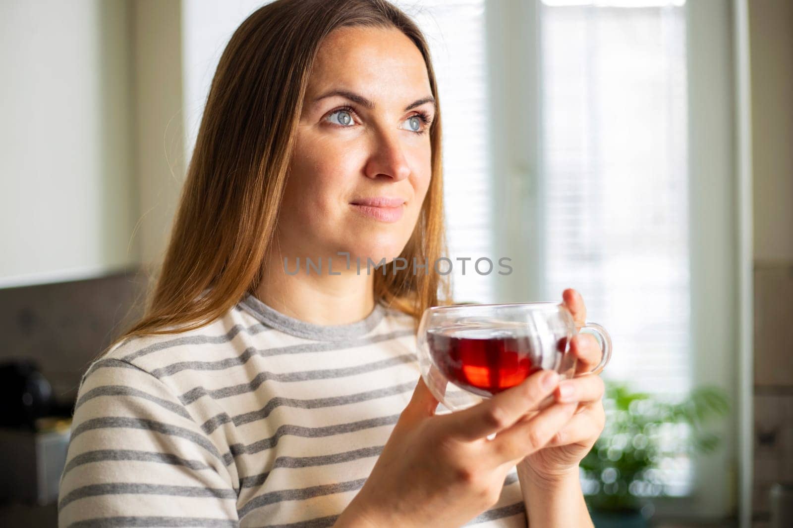 Woman holding a cup of hot tea in the morning. Looking out the window and drinking tea. Good morning with tea