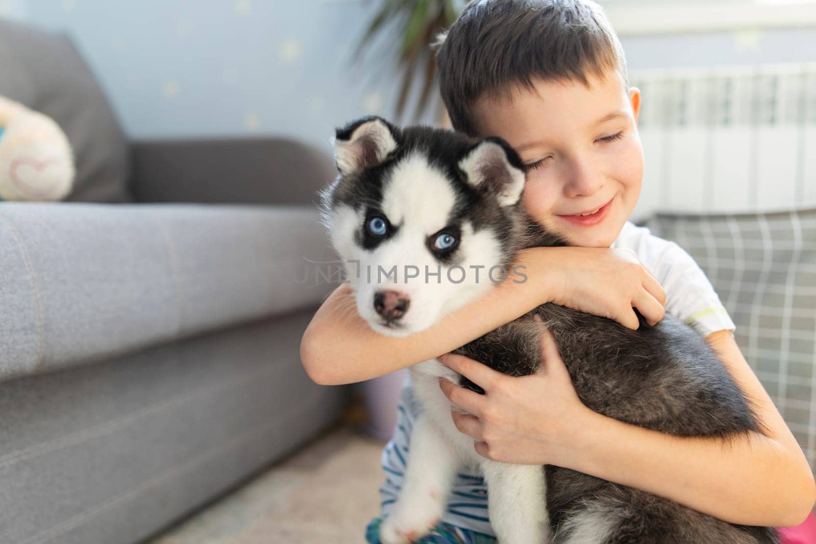 A boy sitting on the floor with his husky puppy. Child hugging his pup. Animal care. Birthday Surprise