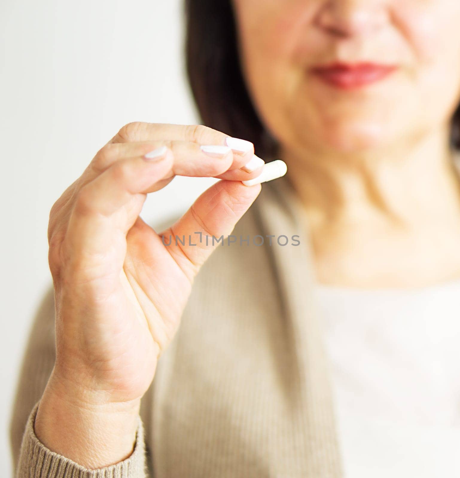 A portrait of a retired woman in casual clothes at home holding her medication. Healthy middle aged 60s woman holding a tablet. Happy adult woman taking vitamin pill.