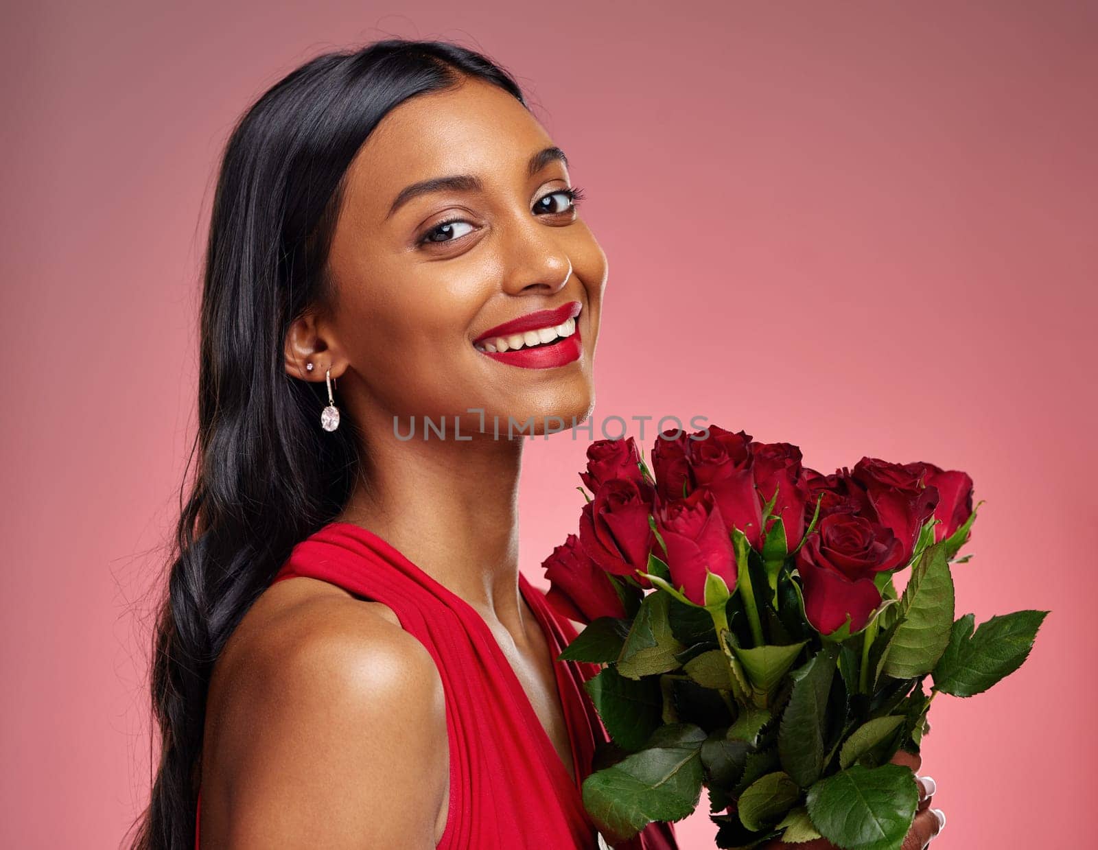 Happy, beauty and portrait of a woman with a rose on a studio background for valentines day. Makeup, model and face of a young Indian girl with a flower bouquet for romance or love on pink backdrop.