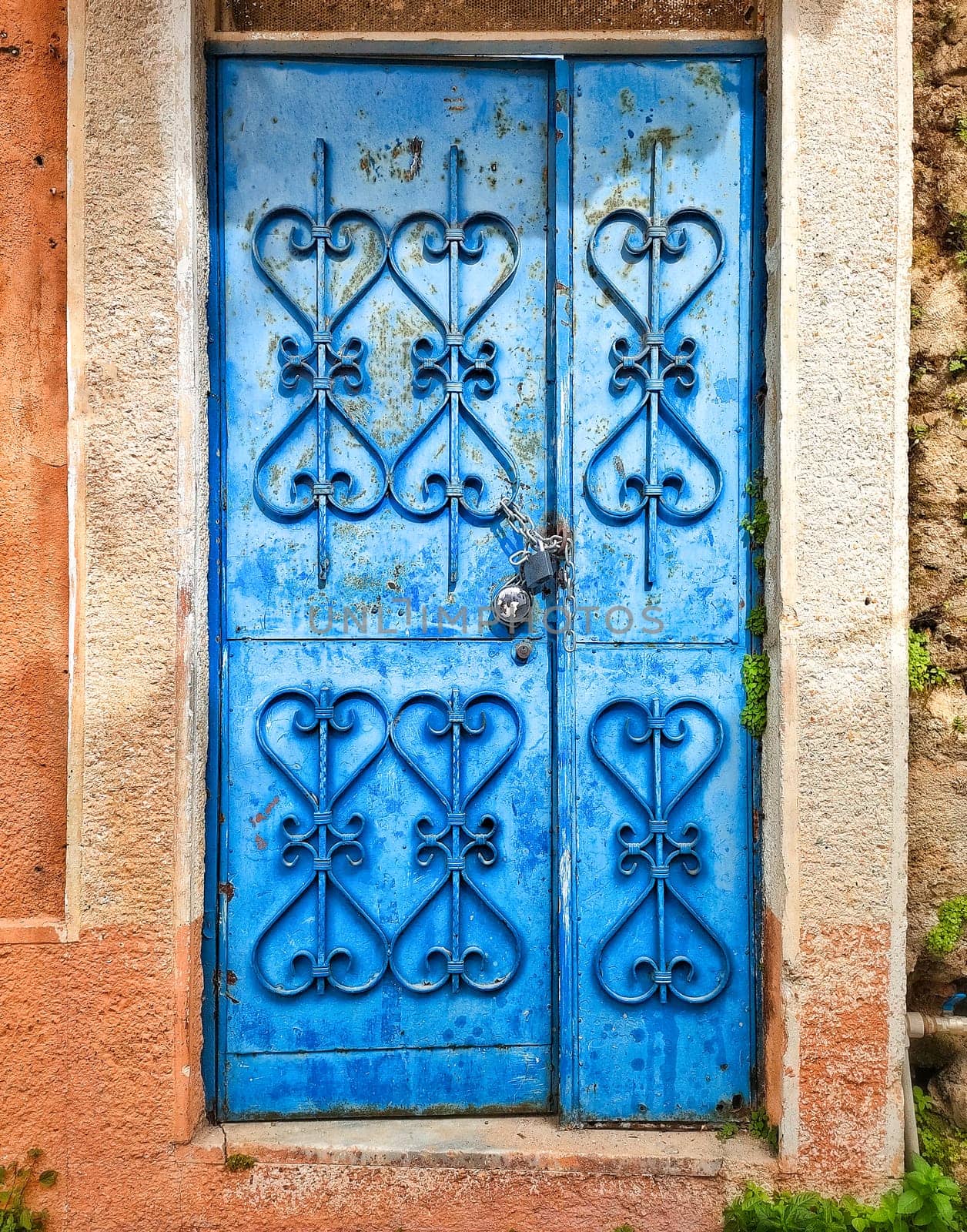 Blue antique door with patterned forging, closed with padlock, against background of stone wall
