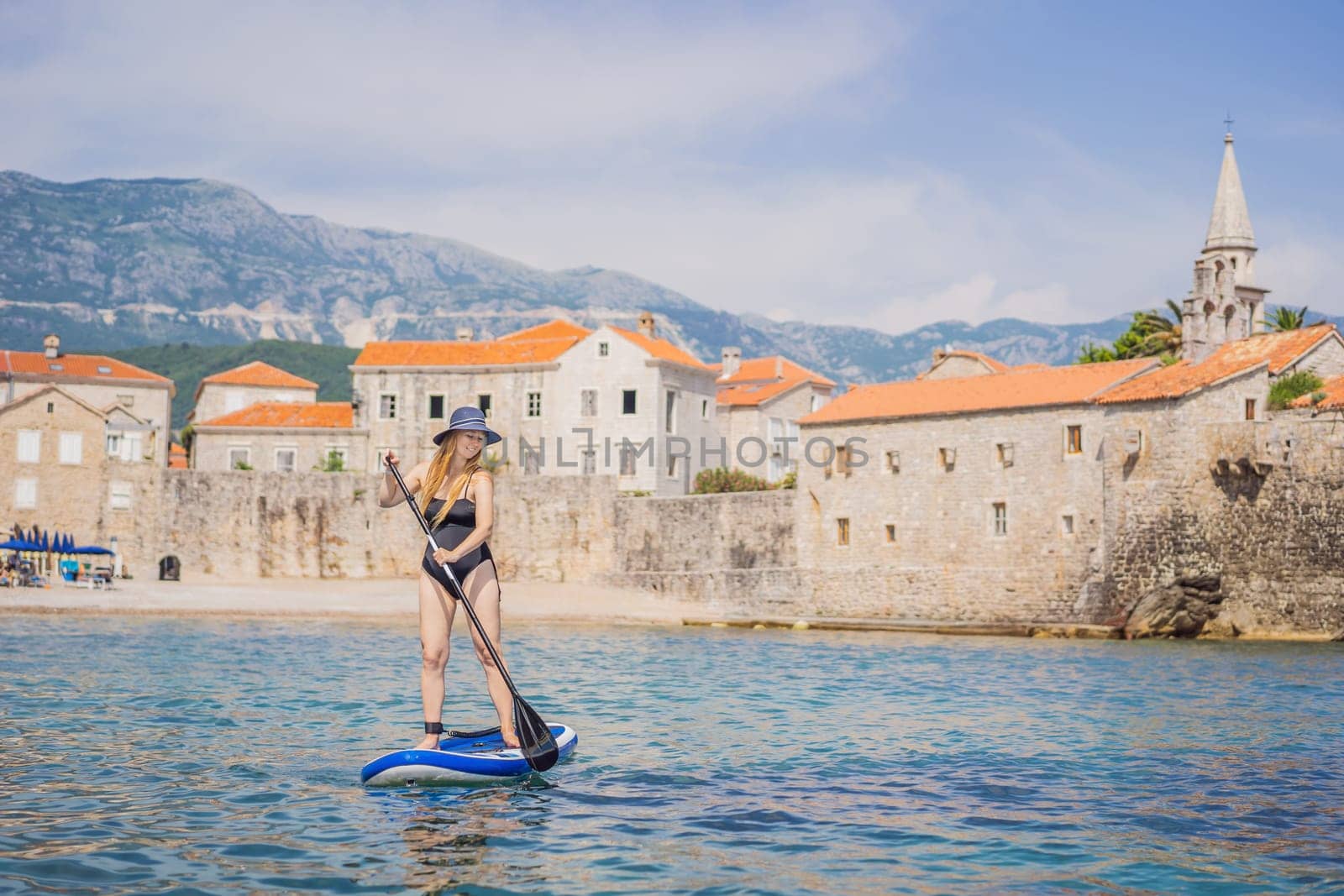 Young women Having Fun Stand Up Paddling in blue water sea in Montenegro. Against the backdrop of the Old Town of Budva. SUP by galitskaya
