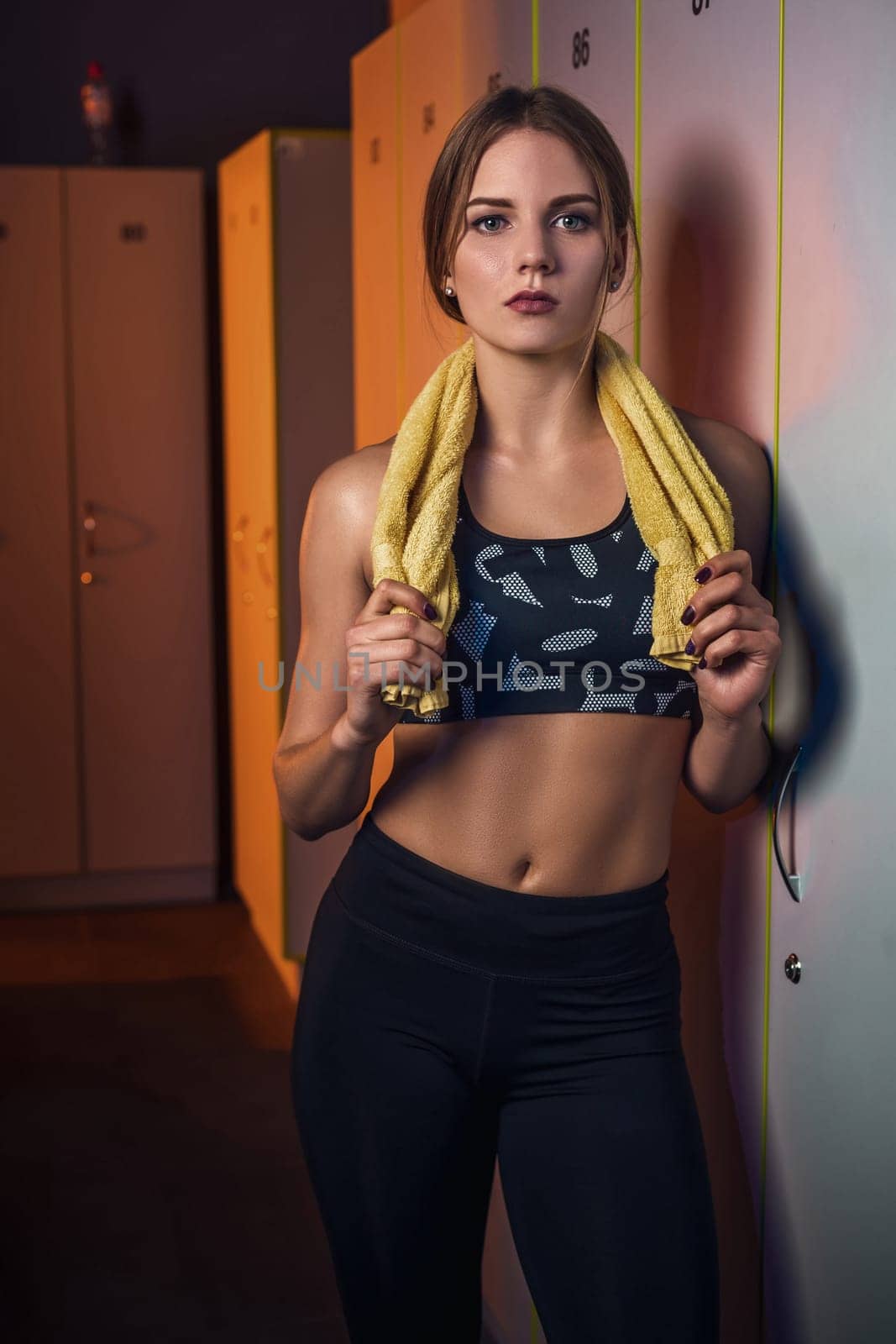 Fitness young beautiful woman with towel resting in dressing room. Dressed in sport clothes. Gym
