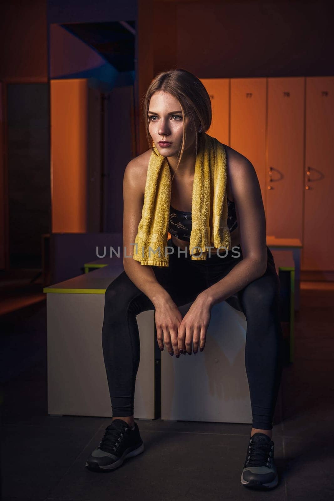 Fitness young beautiful woman with towel resting in dressing room. Dressed in sport clothes. Gym