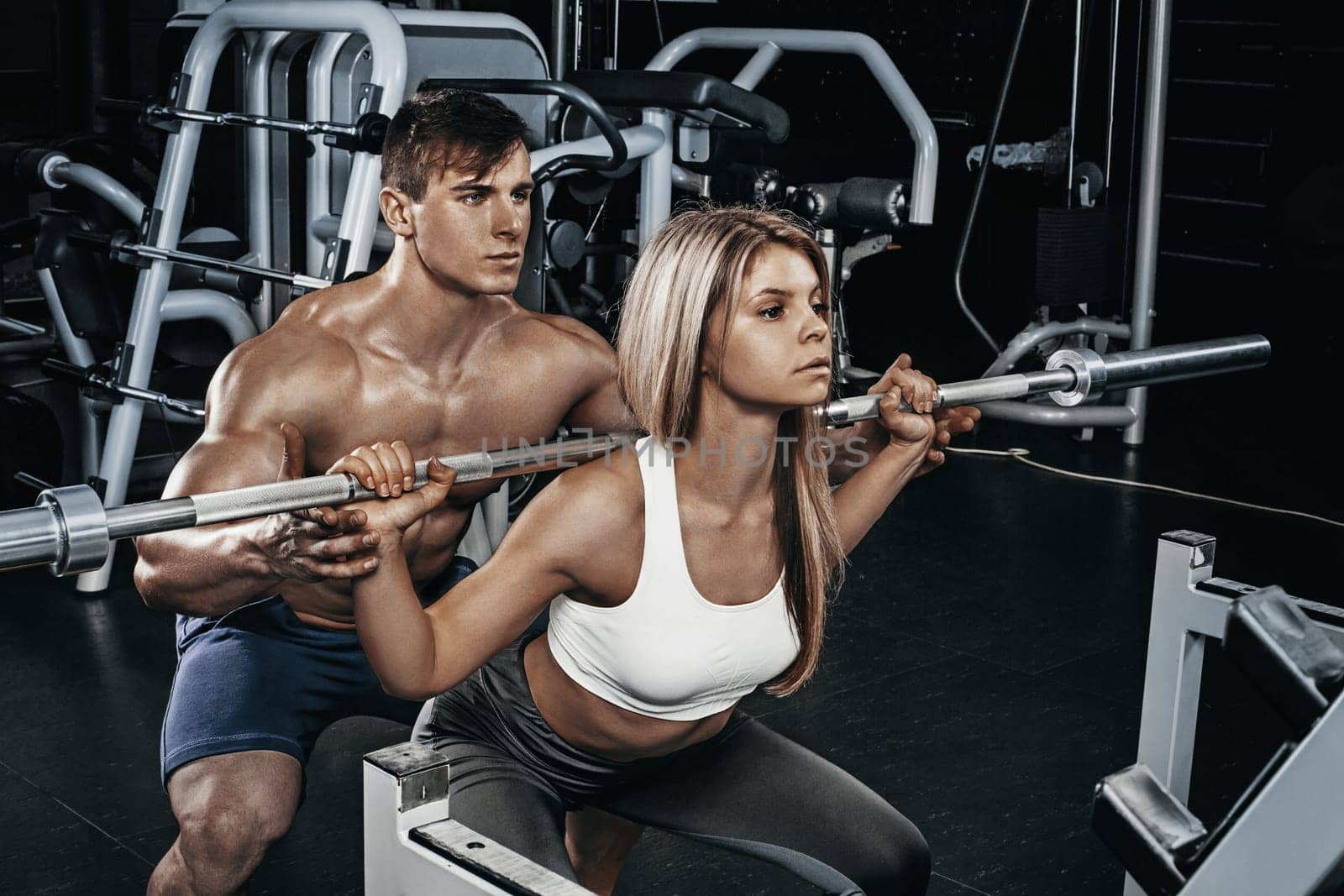 Fitness instructor exercising with his client at the gym. The beautiful blonde is engaged in sports. Handsome man, sports instructor