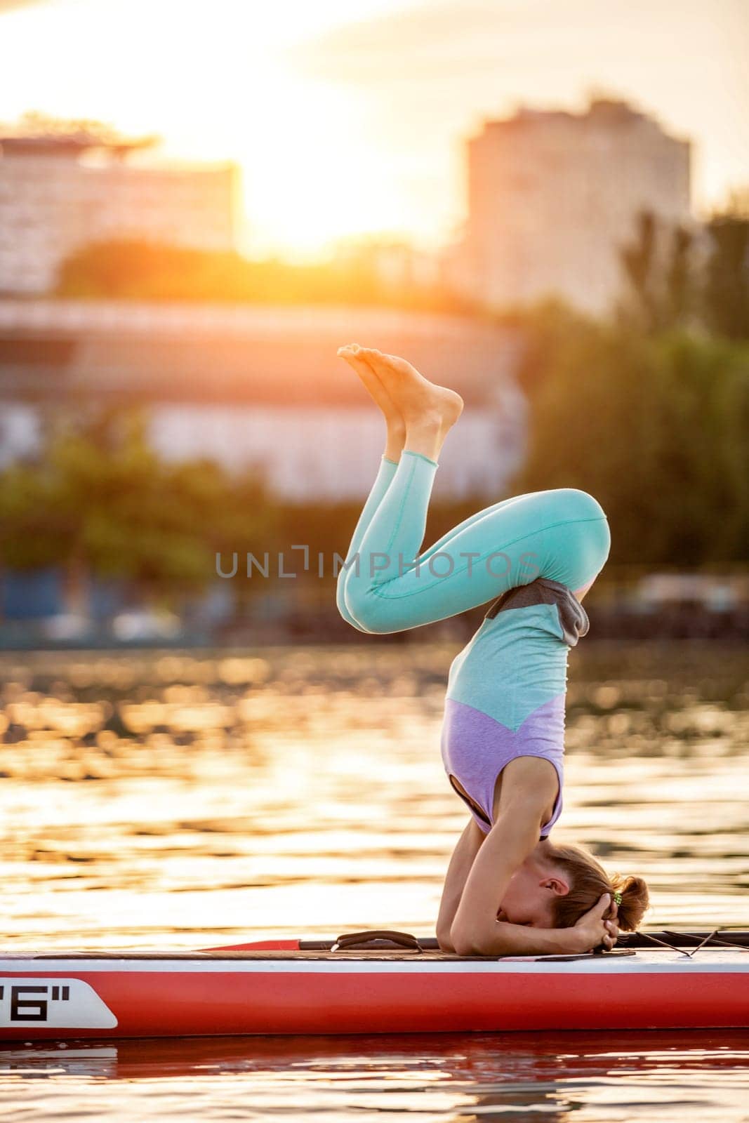 Sporty woman in yoga position on paddleboard, doing yoga on sup board, exercise for flexibility and stretching of muscles. Woman practicing yoga on the paddle board in the morning