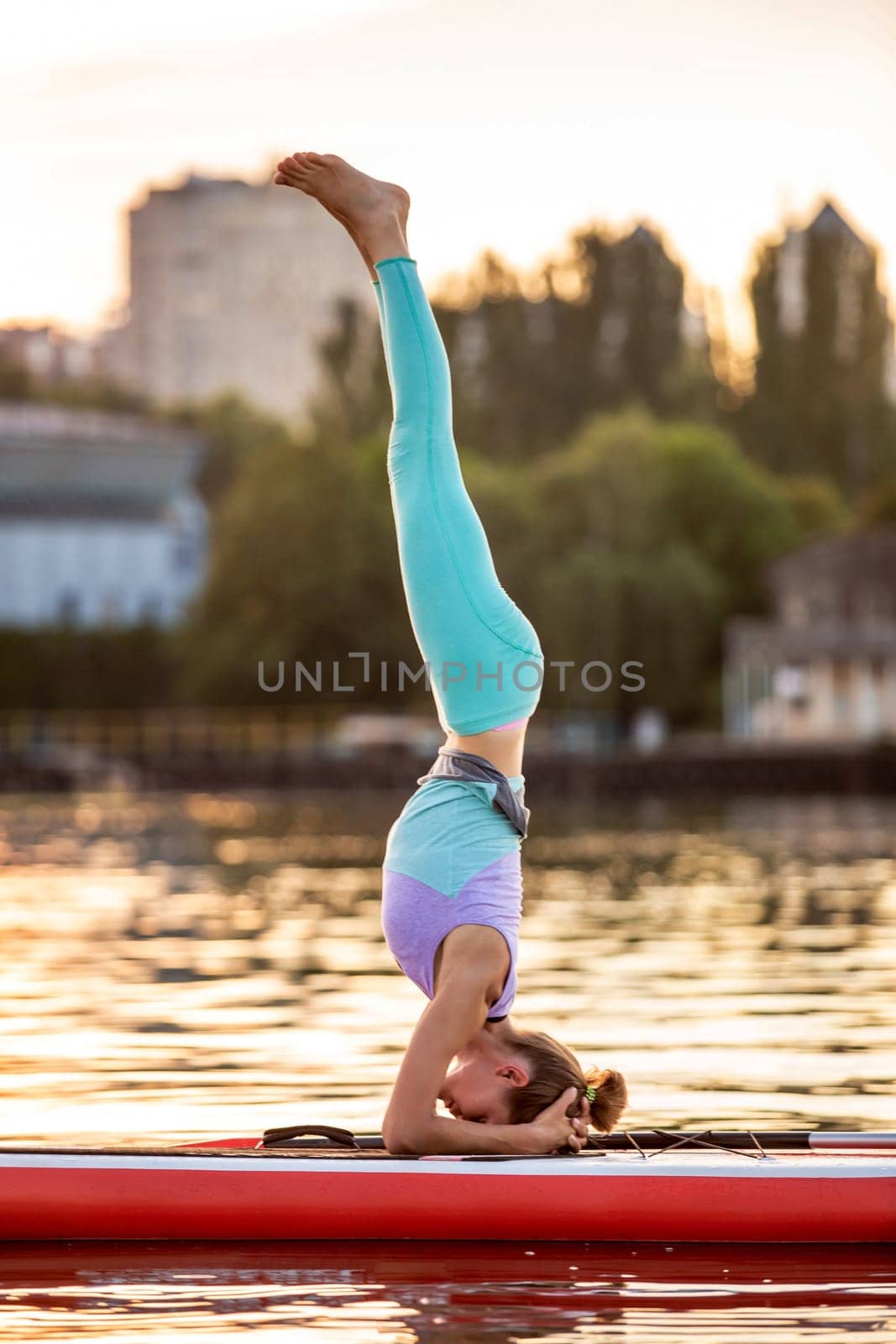 Sporty woman in yoga position on paddleboard, doing yoga on sup board, exercise for flexibility and stretching of muscles. Woman practicing yoga on the paddle board in the morning