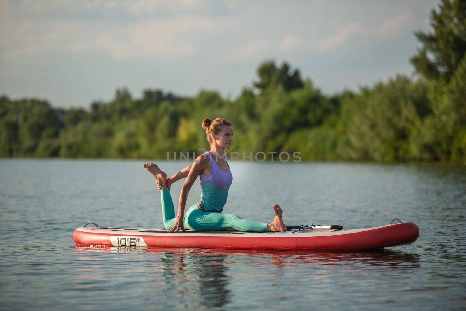 Young woman doing yoga on sup board with paddle. Meditative pose, side view - concept of harmony with the nature, free and healthy living, freelance, remote business.