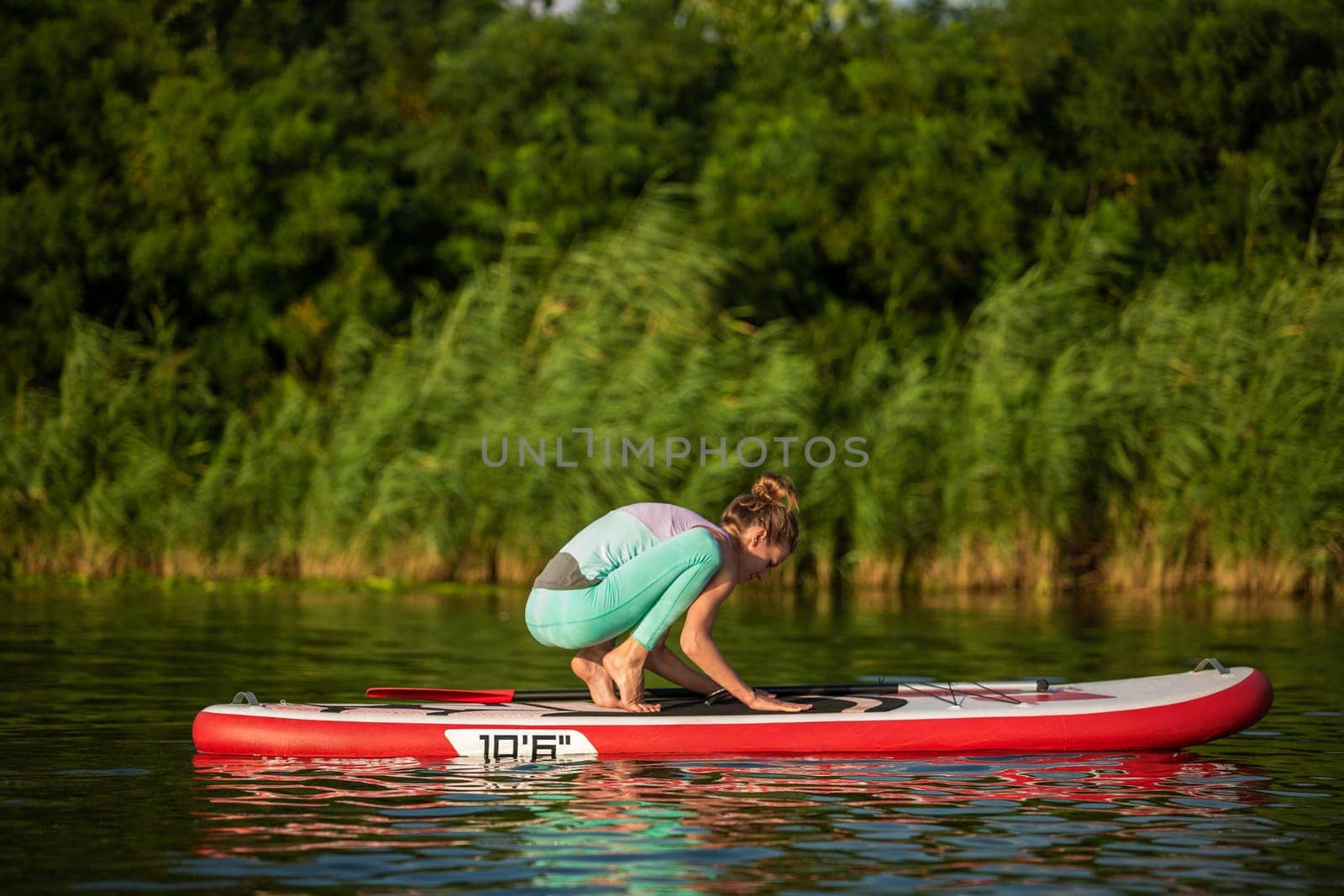 Young woman are doing yoga on a stand up paddle board SUP on a beautiful lake or river. The concept of a healthy lifestyle. Sport. Yoga. Hobby